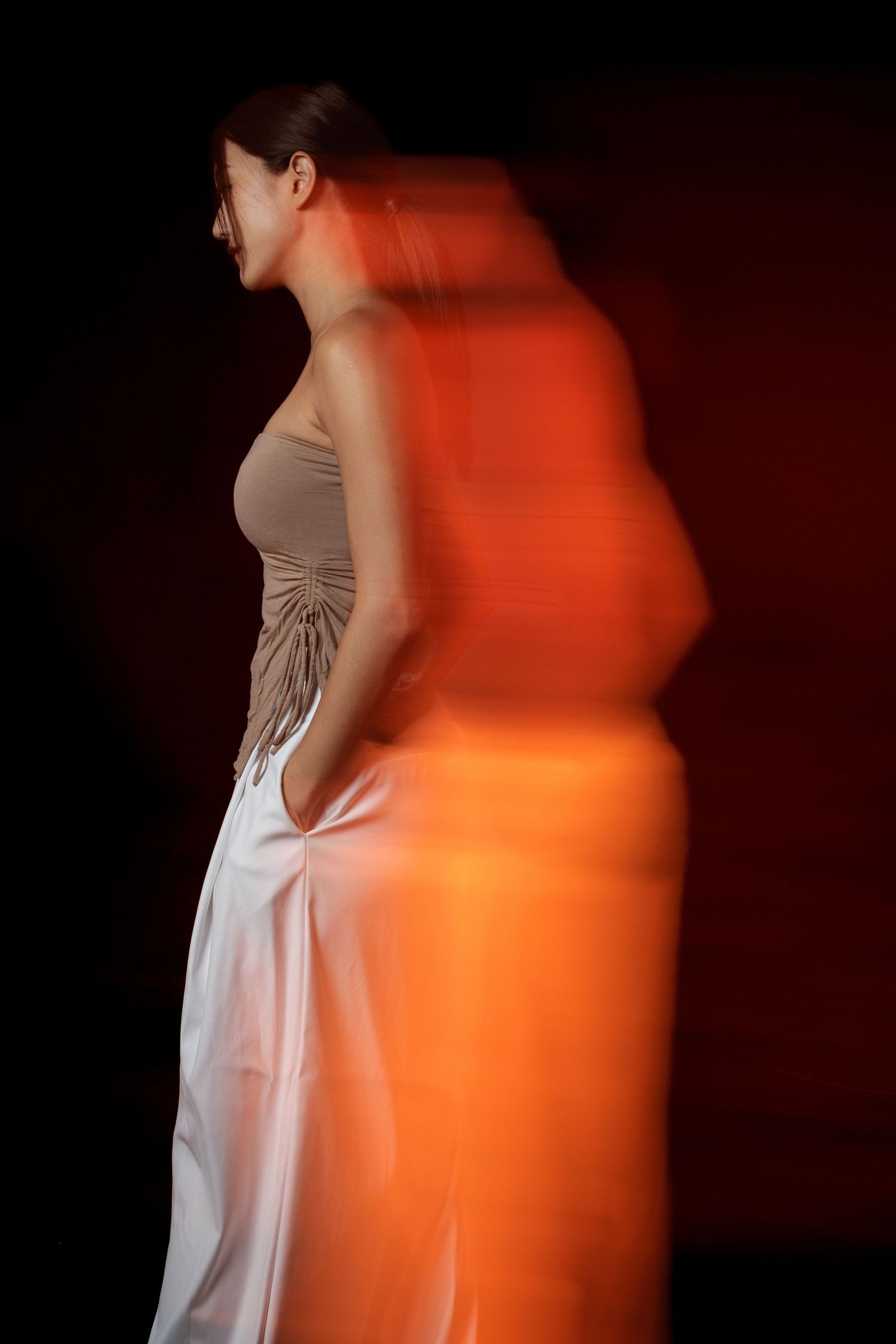 Woman in beige top and white skirt poses with motion blur effect against dark red background.