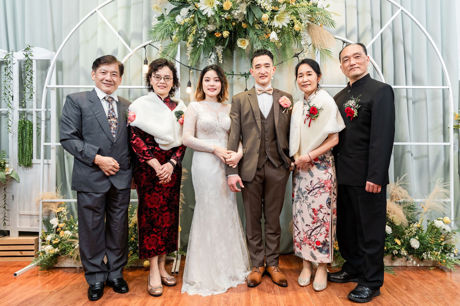 A formal group photo at a wedding ceremony in front of an archway decorated with floral arrangements.