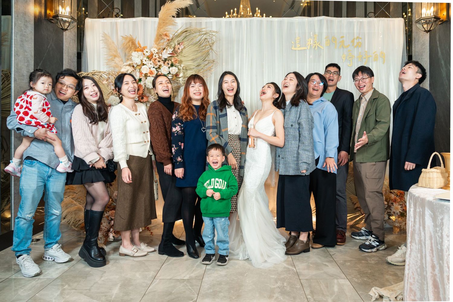 A group of guests pose together at an indoor wedding celebration in formal and casual attire.