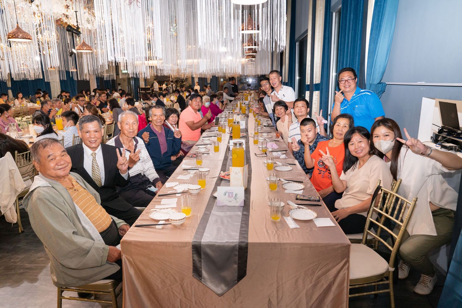 Large group of people sitting at a long table covered with brown tablecloth during a formal dinner gathering.
