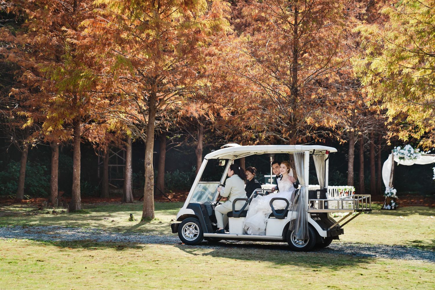 White golf cart transporting wedding party through scenic autumn landscape.