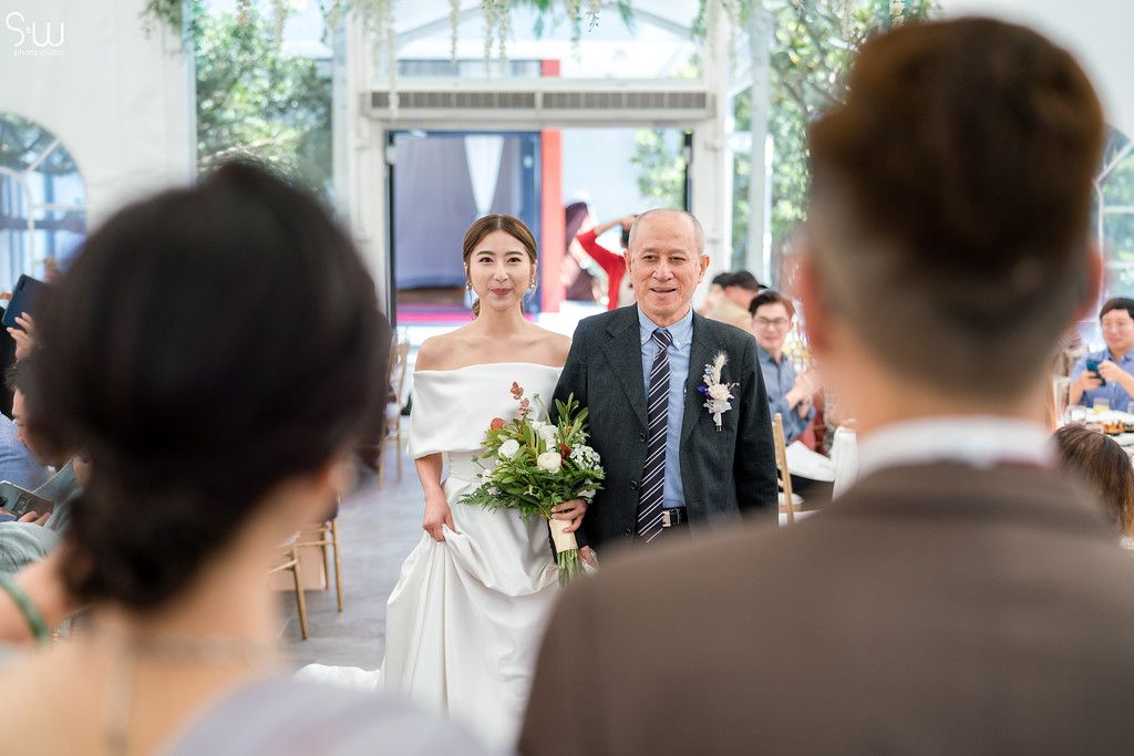 Wedding processional in light-filled venue with hanging greenery decorations.