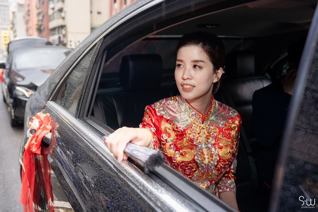 A bride in a red and gold traditional Chinese dress looks out from a decorated wedding car.