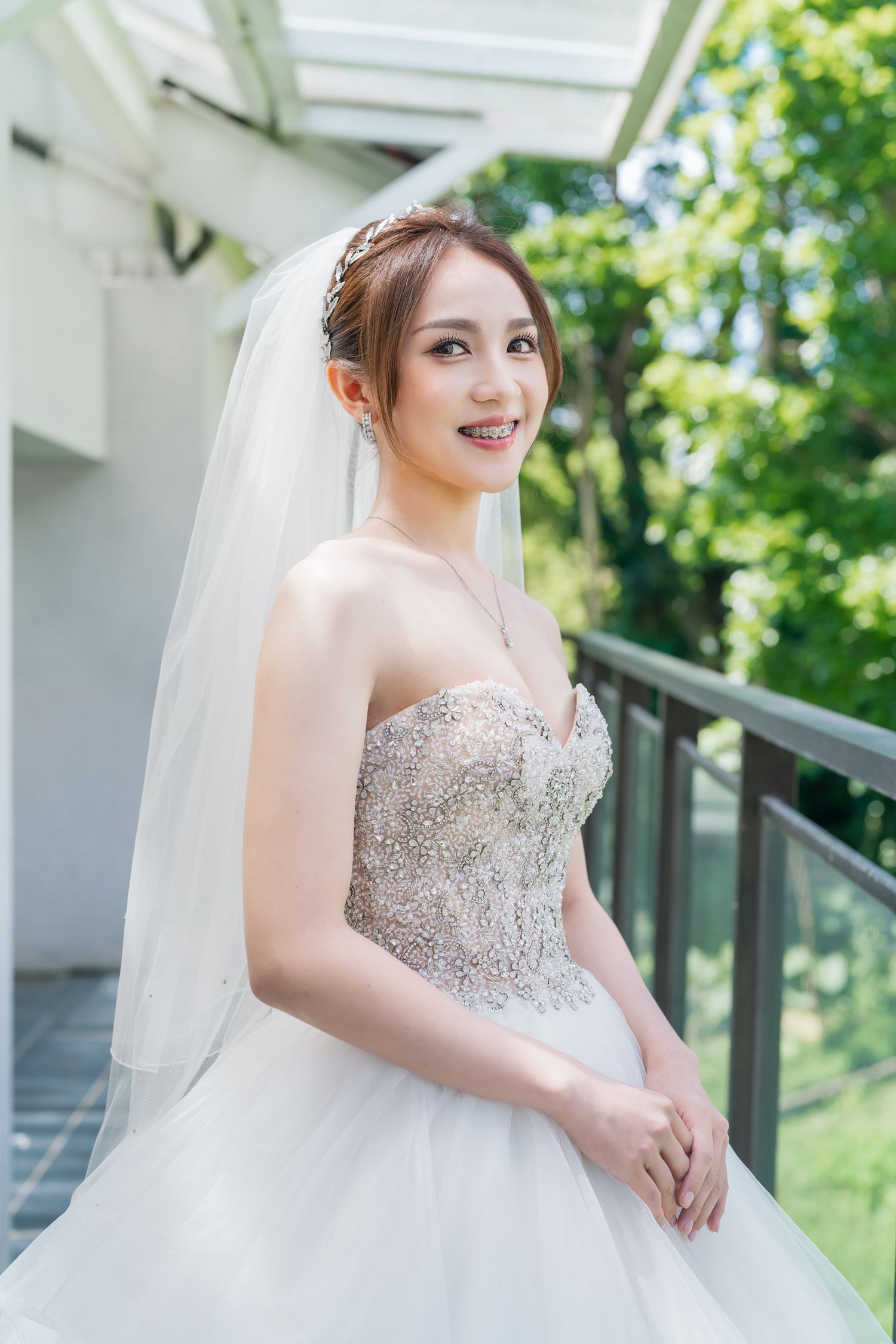 Smiling bride in beaded strapless gown and veil poses on modern outdoor terrace.