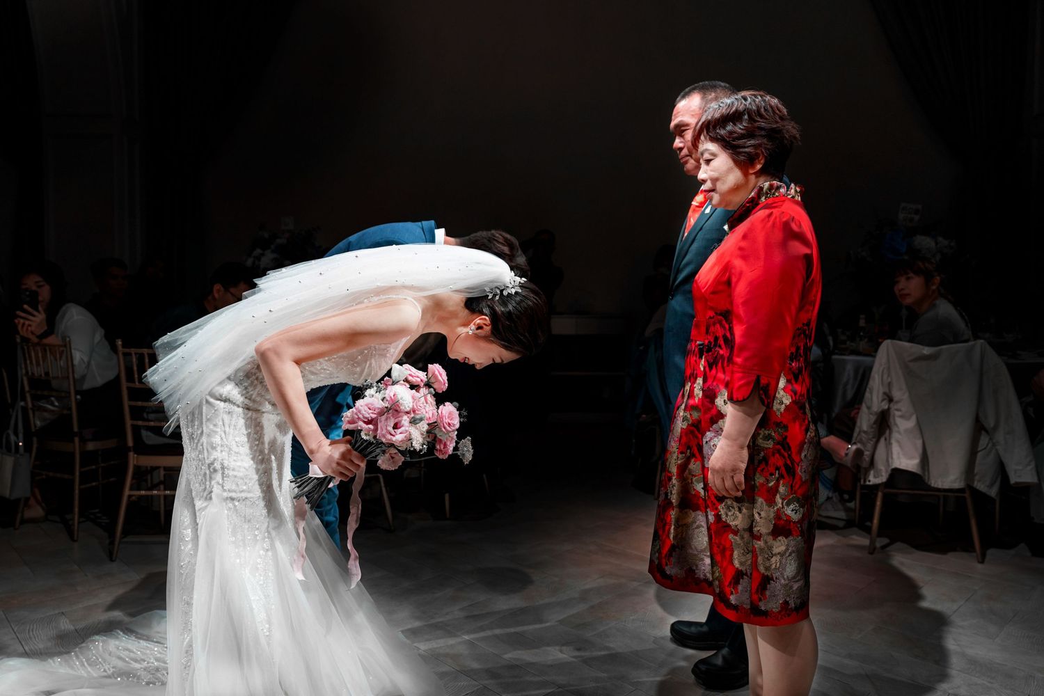 Atmospheric wedding scene with a bride in white gown bowing before a person in a red outfit amid theatrical fog.