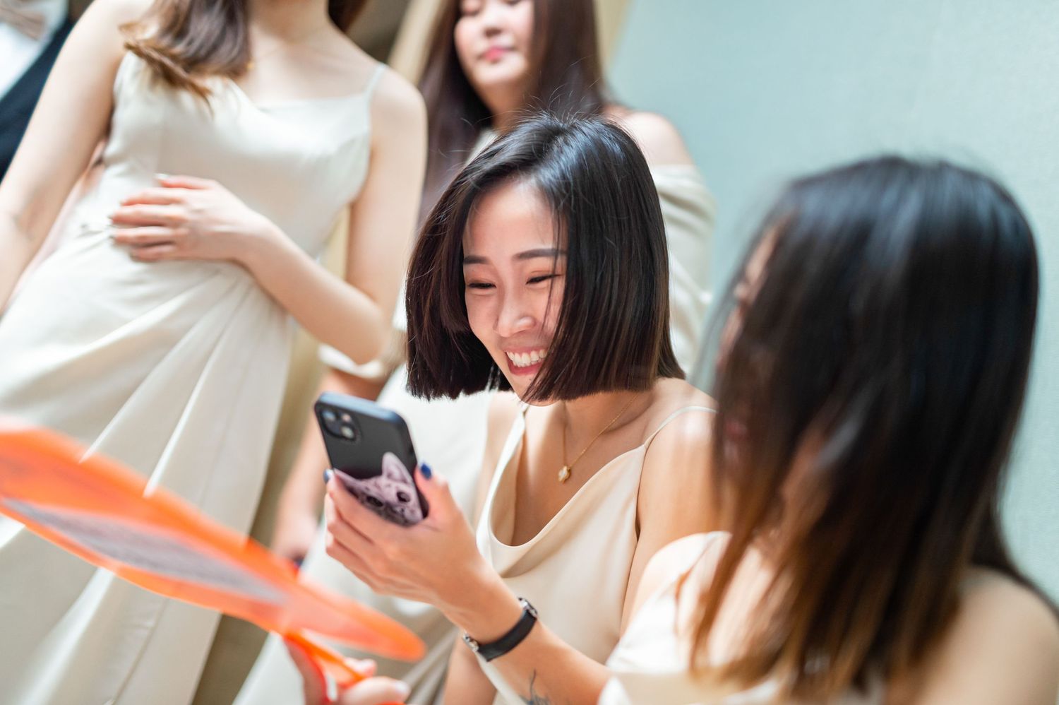 Group of friends in white dresses gather together to look at something amusing on a mobile phone.