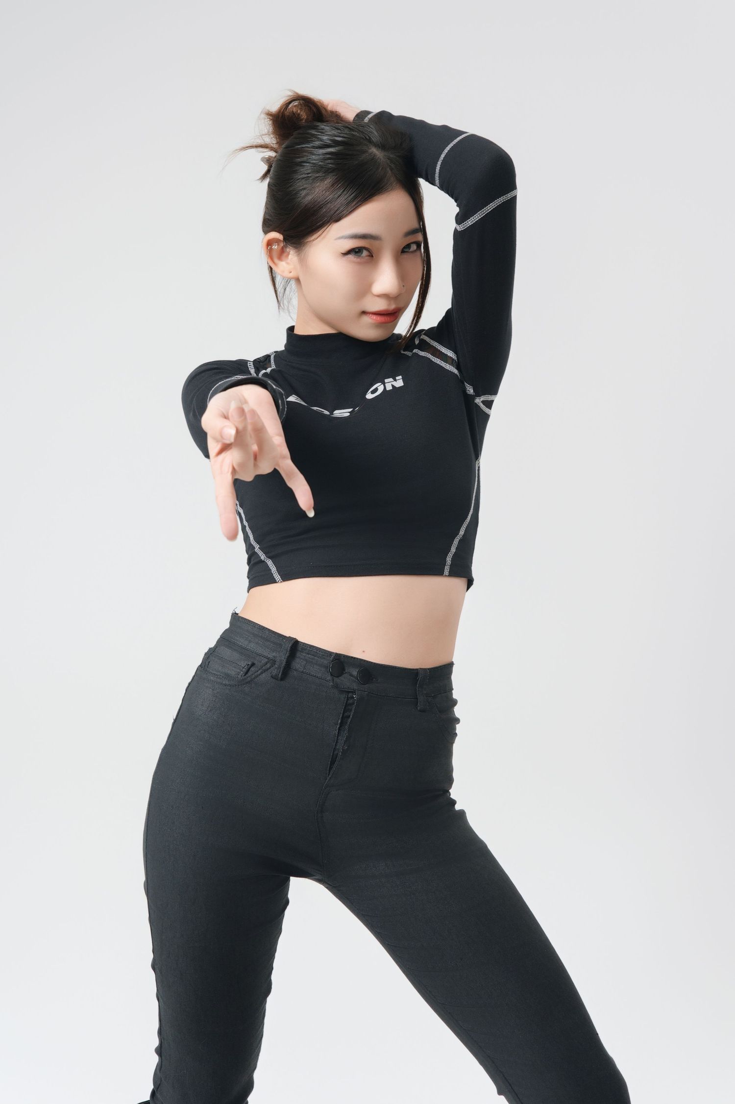 Young woman in black crop top and pants strikes a dynamic dance pose against a white background.