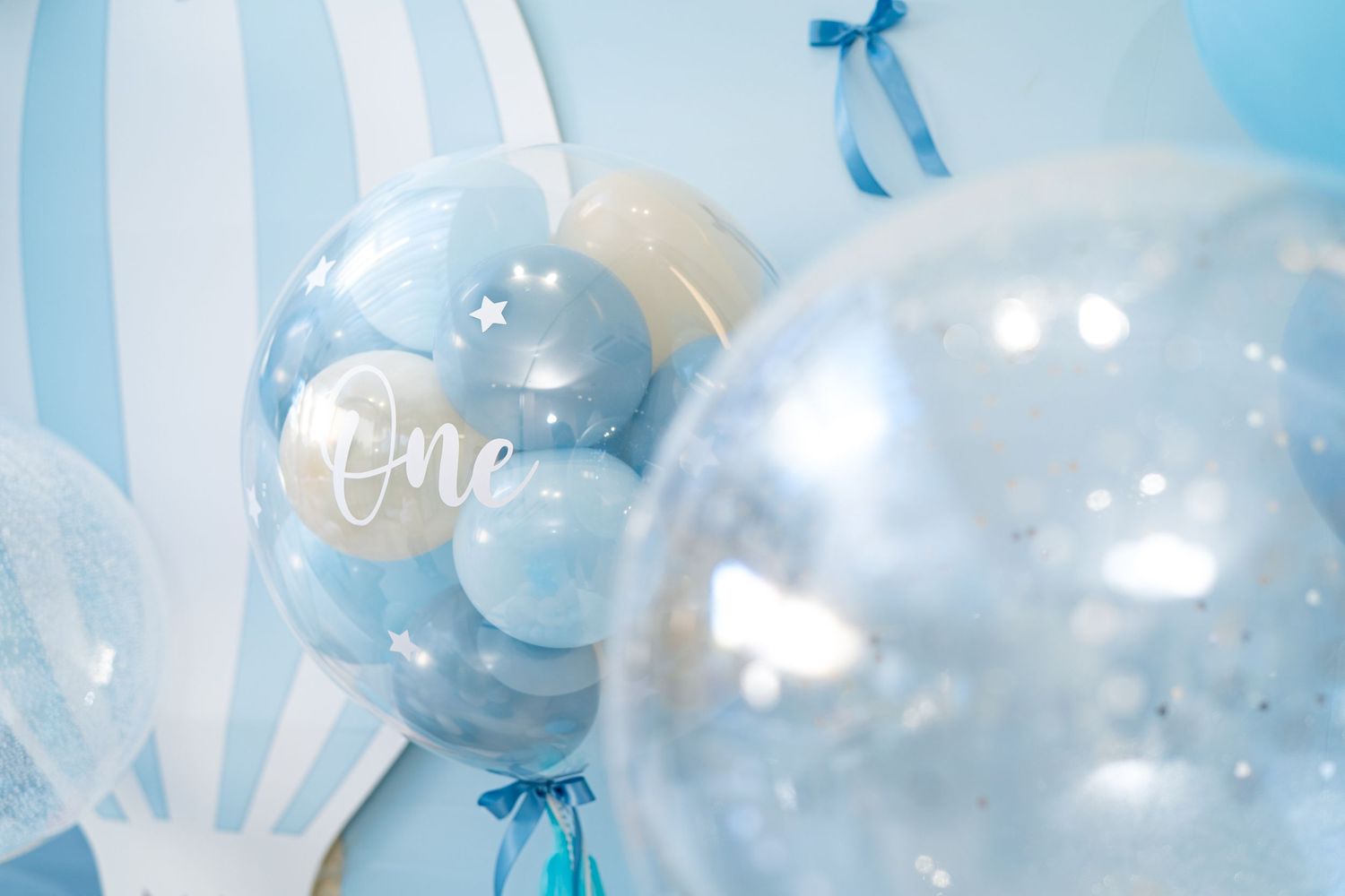 Light blue and white balloon decorations with bows create an elegant party atmosphere against a white background.