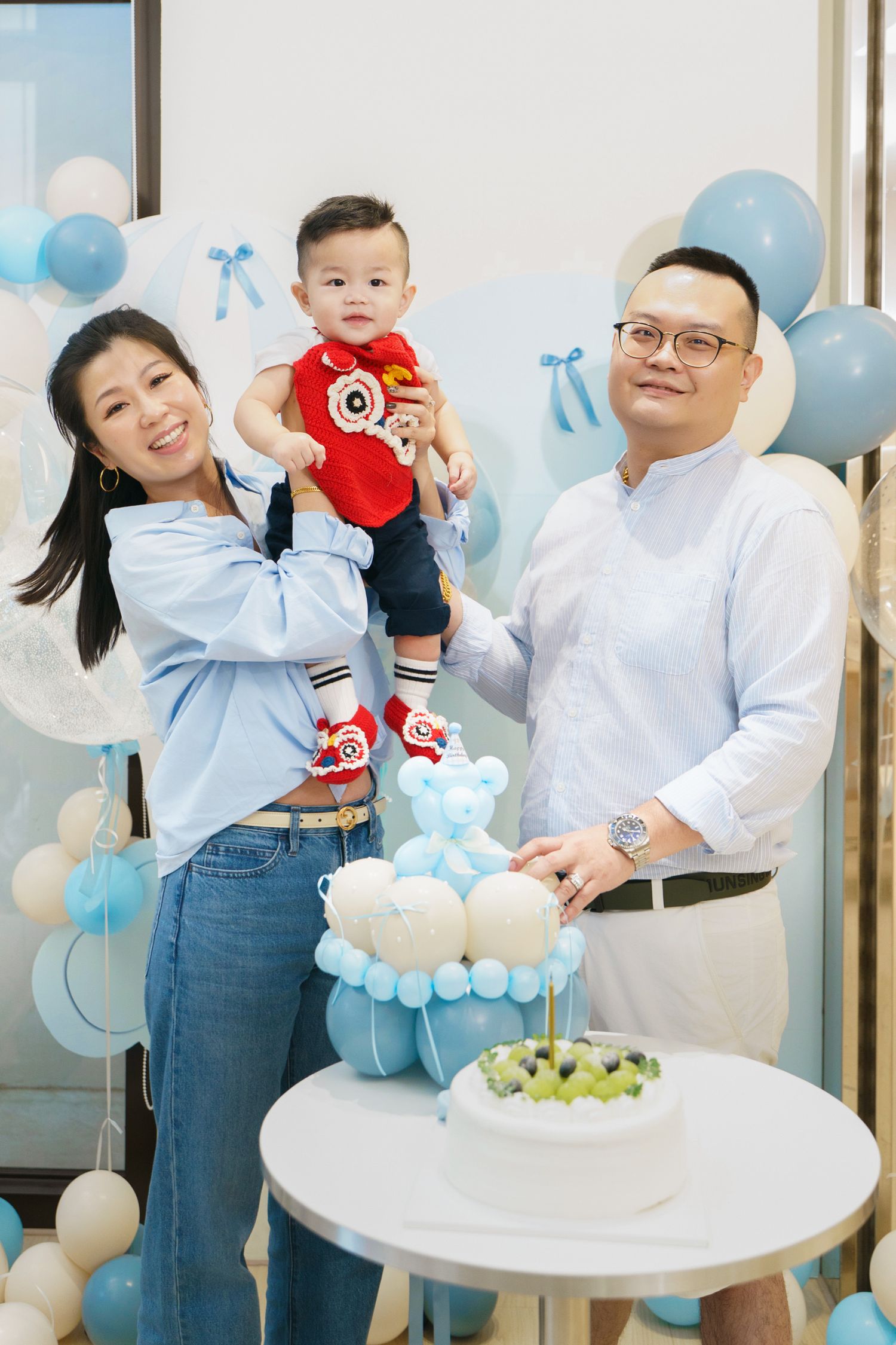 Family celebrating at a baby shower with blue and white balloon decorations and round tables with party decor.