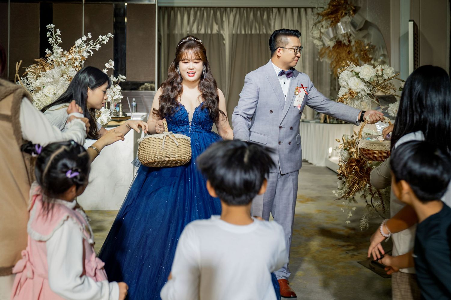 Wedding guests gather around tables decorated with floral centerpieces during an elegant indoor reception celebration.