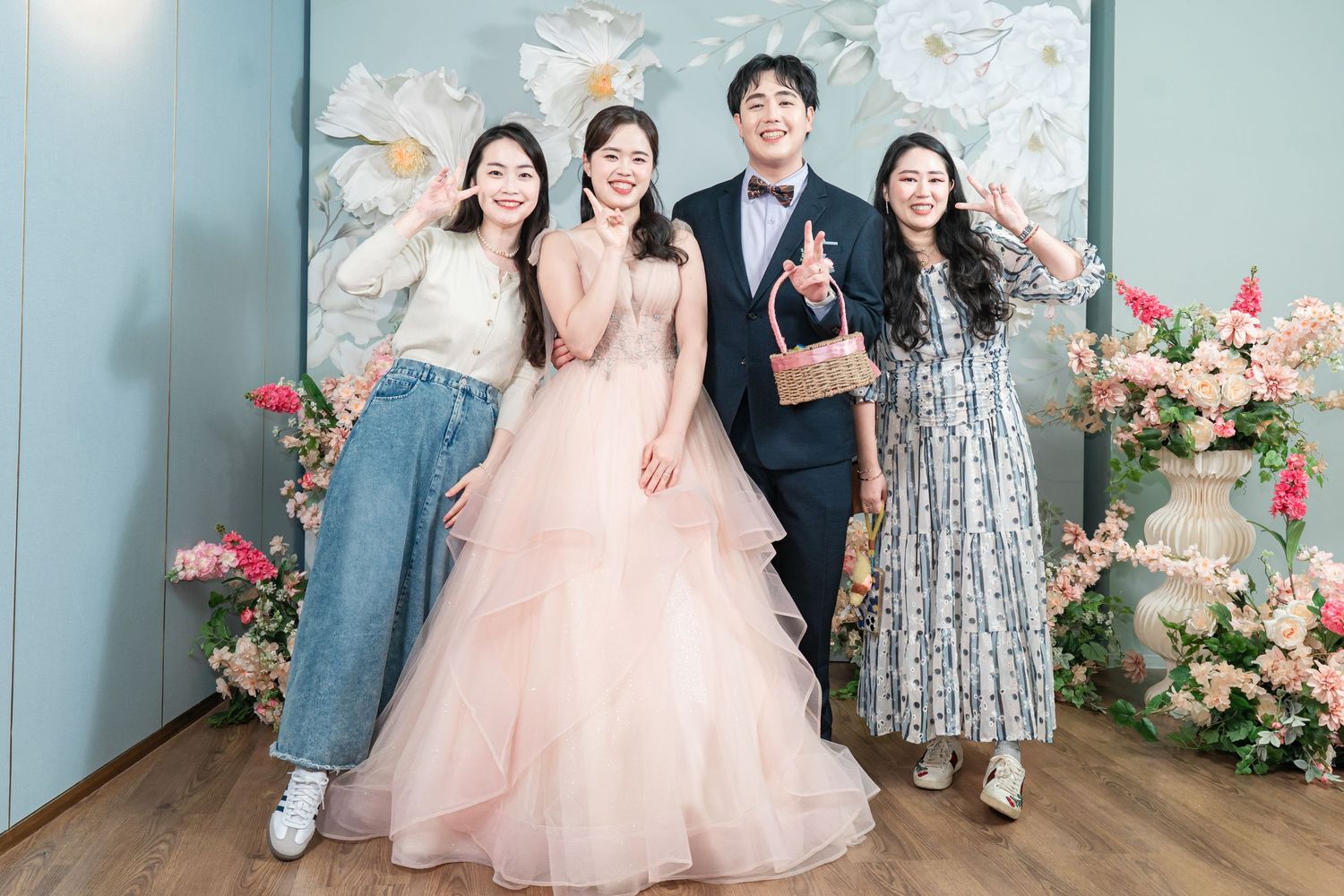 A group poses together in formal attire against a blue wall with pink floral decorations.