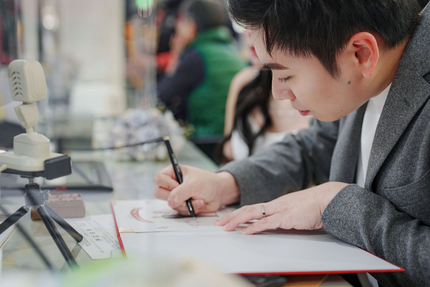Student in gray uniform writes with pencil at desk while studying in classroom.