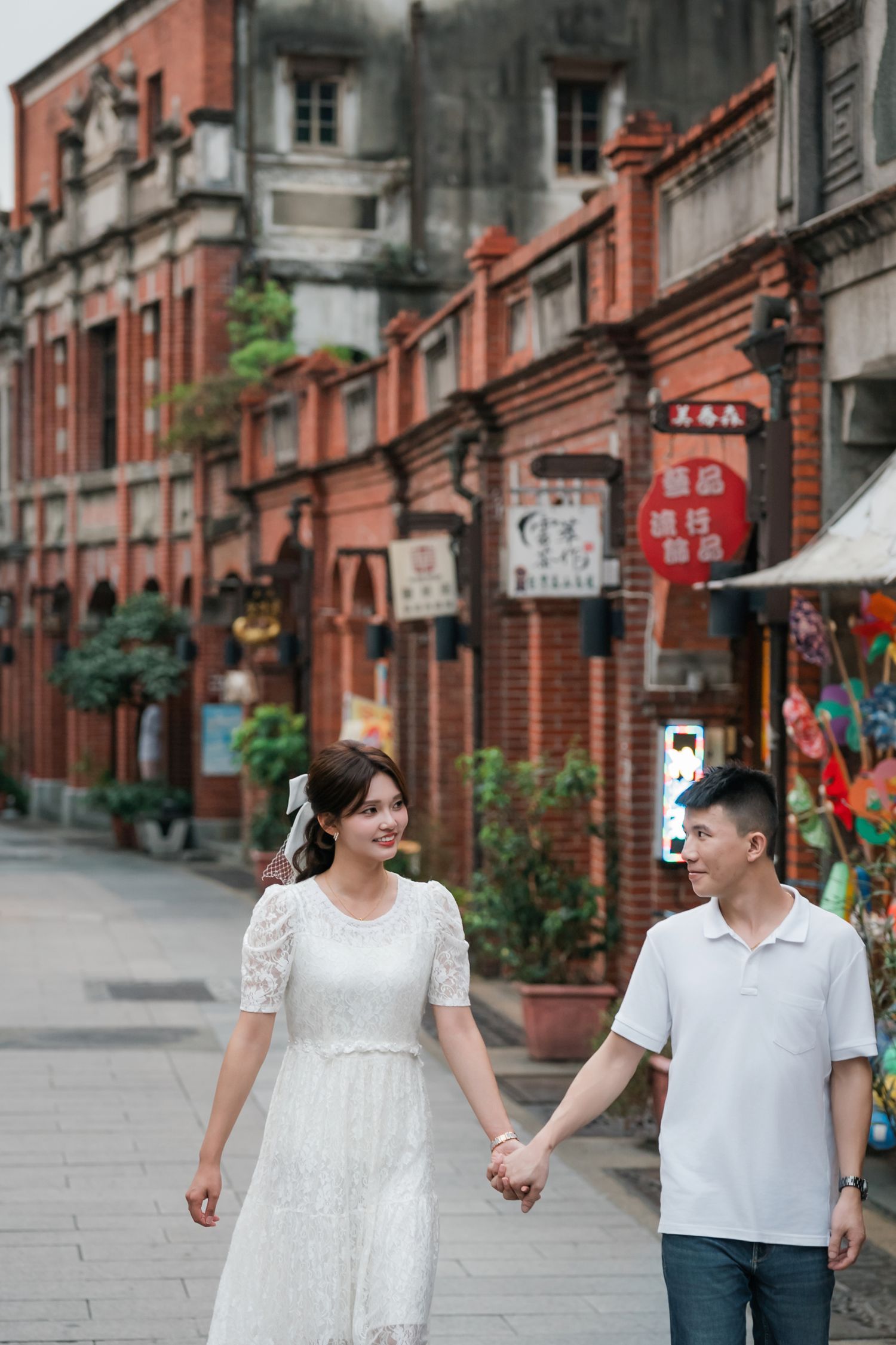 A couple walks hand in hand down a historic street lined with red brick buildings and Chinese signage.