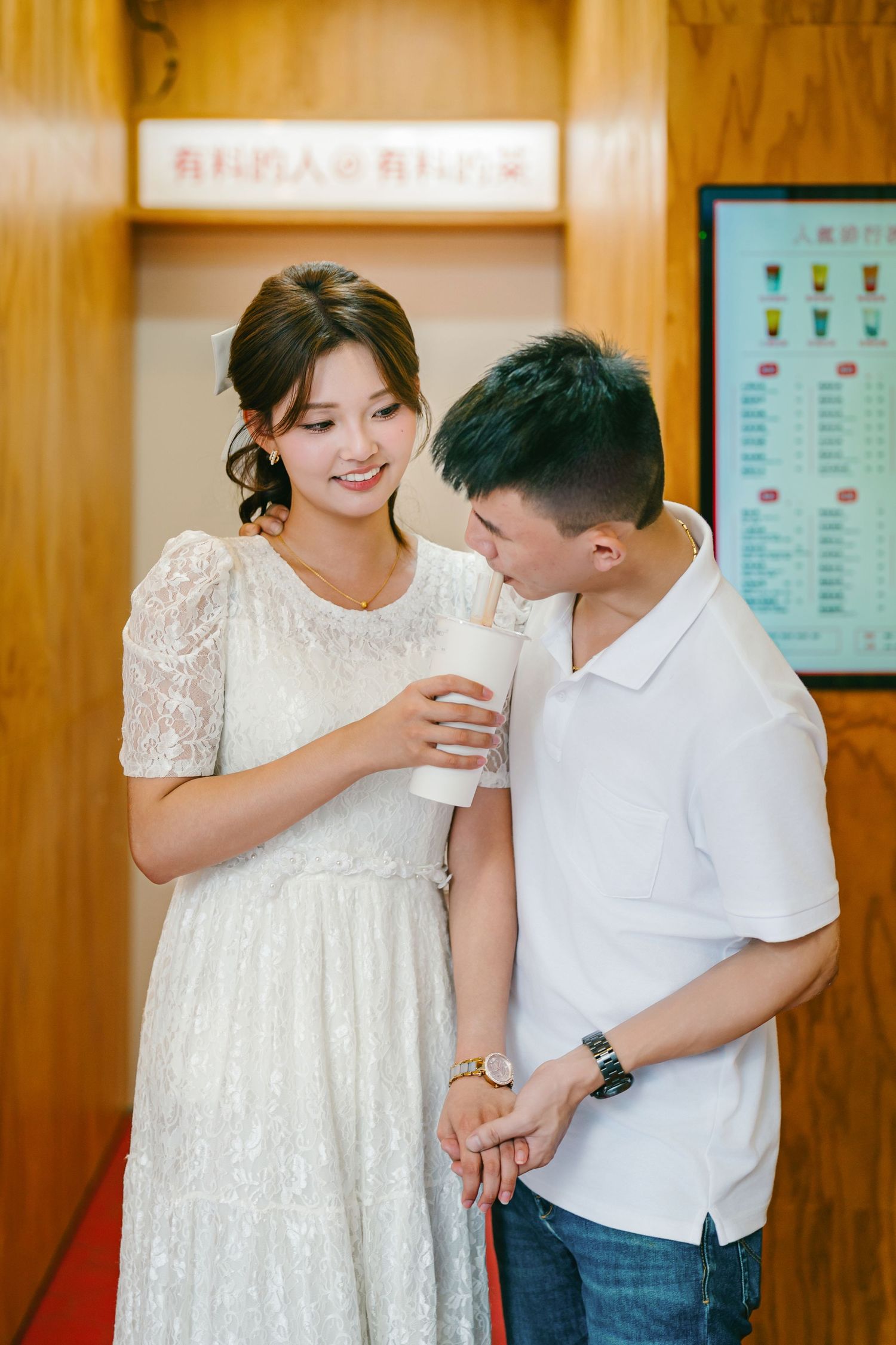 A couple shares a tender moment in matching white outfits against a wooden wall backdrop.