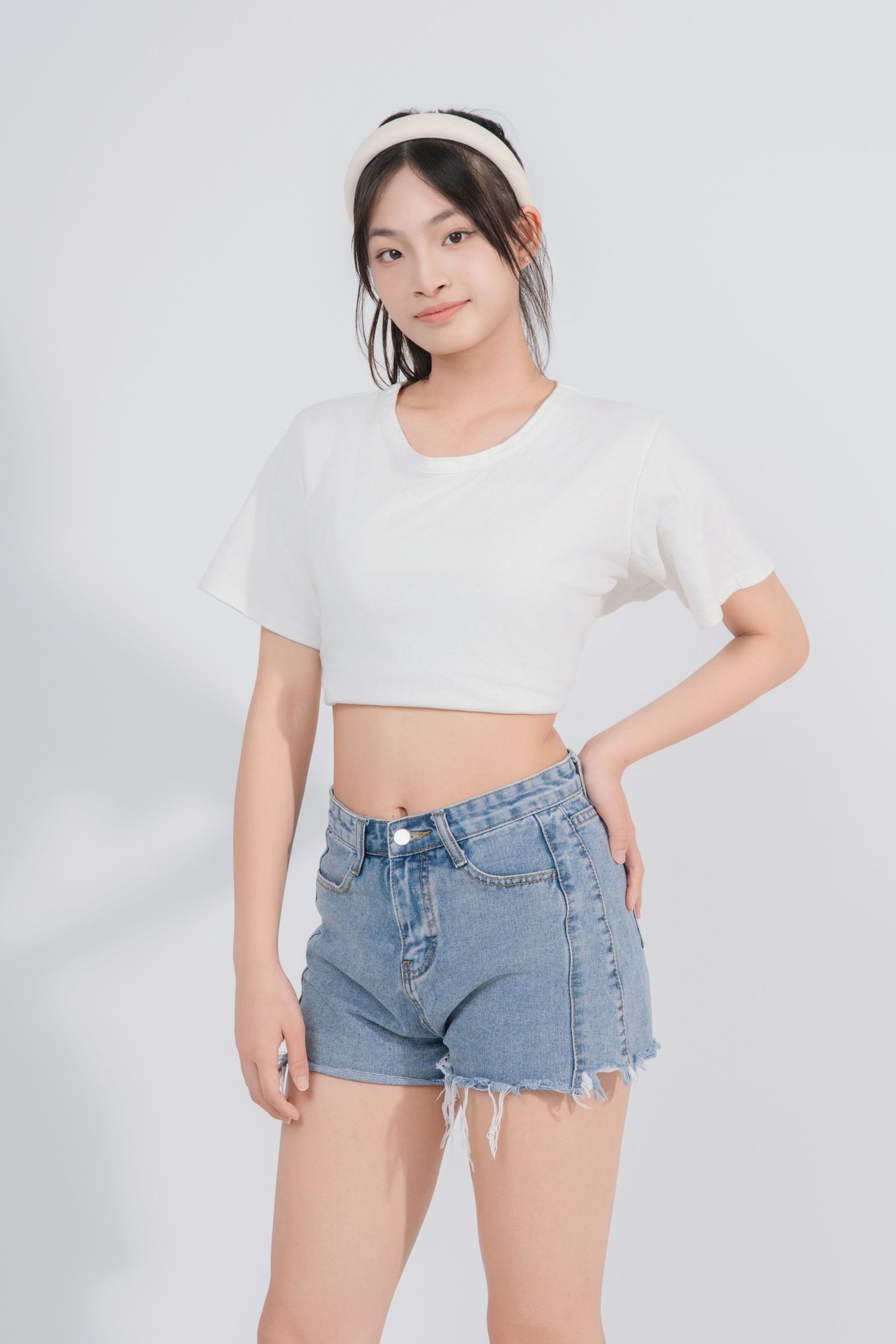 A person in a white crop top and distressed denim shorts poses against a light background.