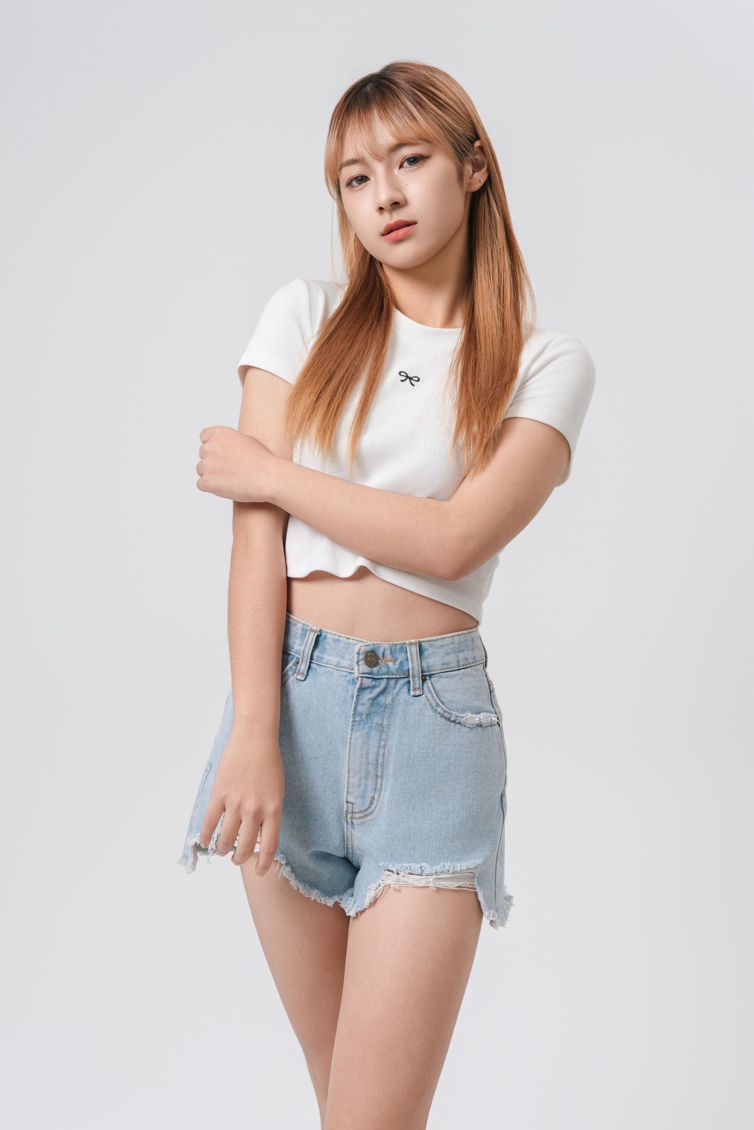A person in a white crop top and light blue denim shorts poses against a white background.