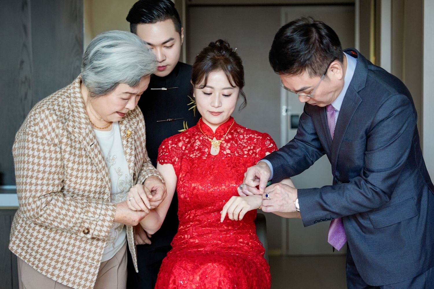 A traditional Chinese tea ceremony shows people in formal attire gathered around a person wearing a red qipao dress.