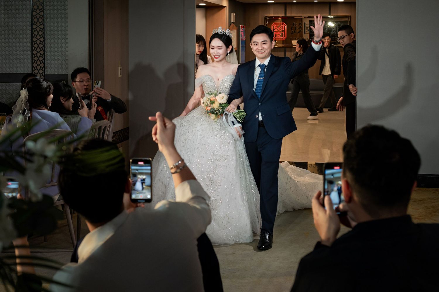 A couple shares their first dance at a wedding reception while guests watch and take photos on their phones.