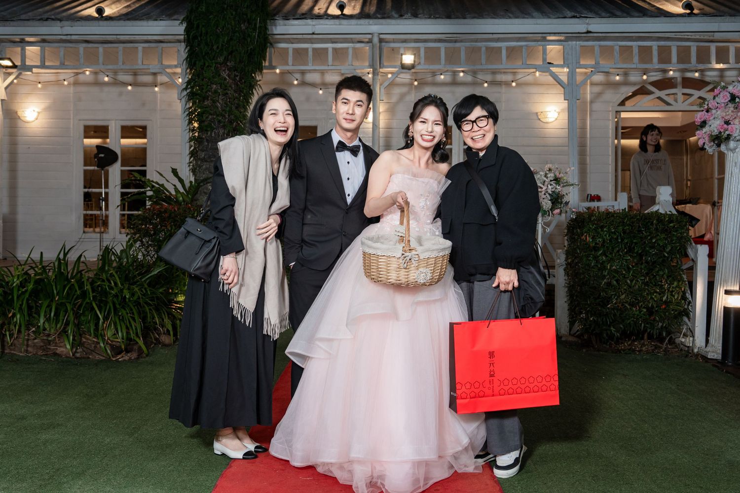 Wedding party poses together outside venue with string lights and greenery in the background.