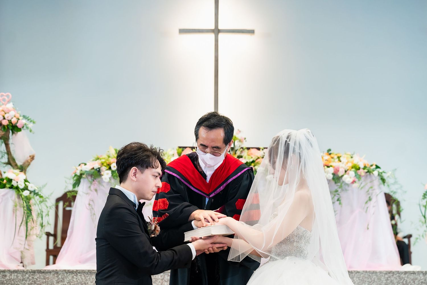 Wedding ceremony with officiant and couple at decorated altar under illuminated cross.