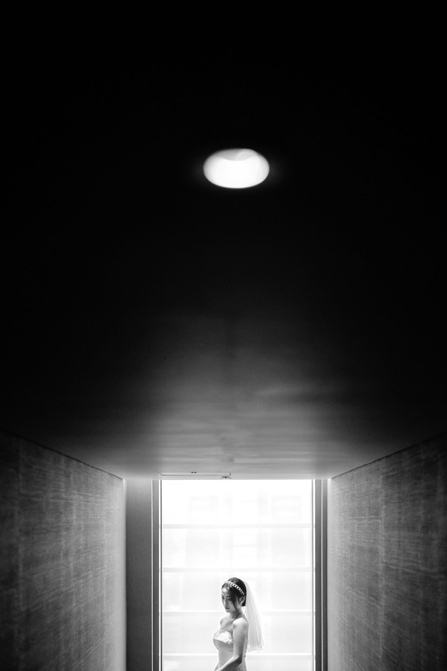 A silhouette stands in a bright doorway at the end of a dark corridor with dramatic overhead lighting.