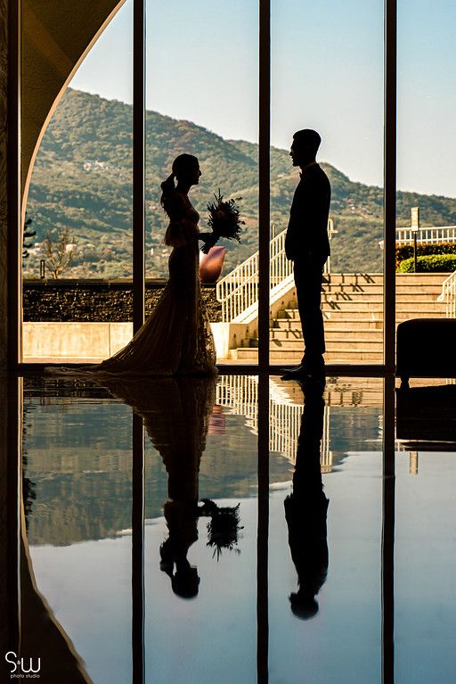 Silhouetted wedding couple against mountain view through large windows creating dramatic reflection.