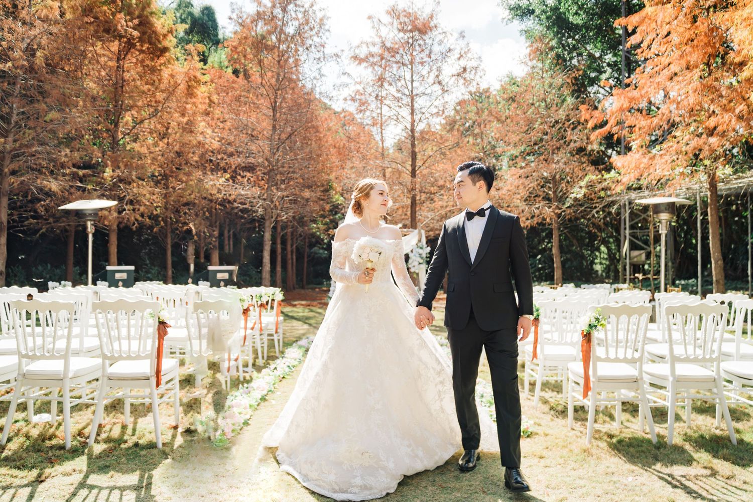 Wedding ceremony setup outdoors with white chairs and golden fall foliage creating a romantic autumn atmosphere.