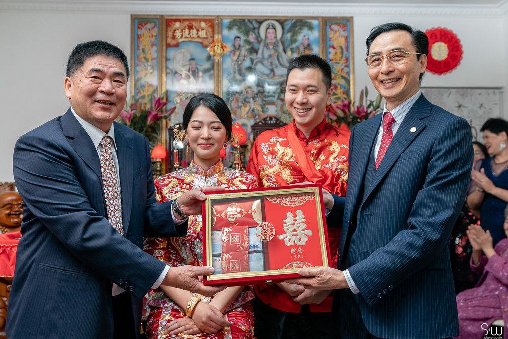 Wedding guests present a traditional red gift box during Chinese tea ceremony celebrations.