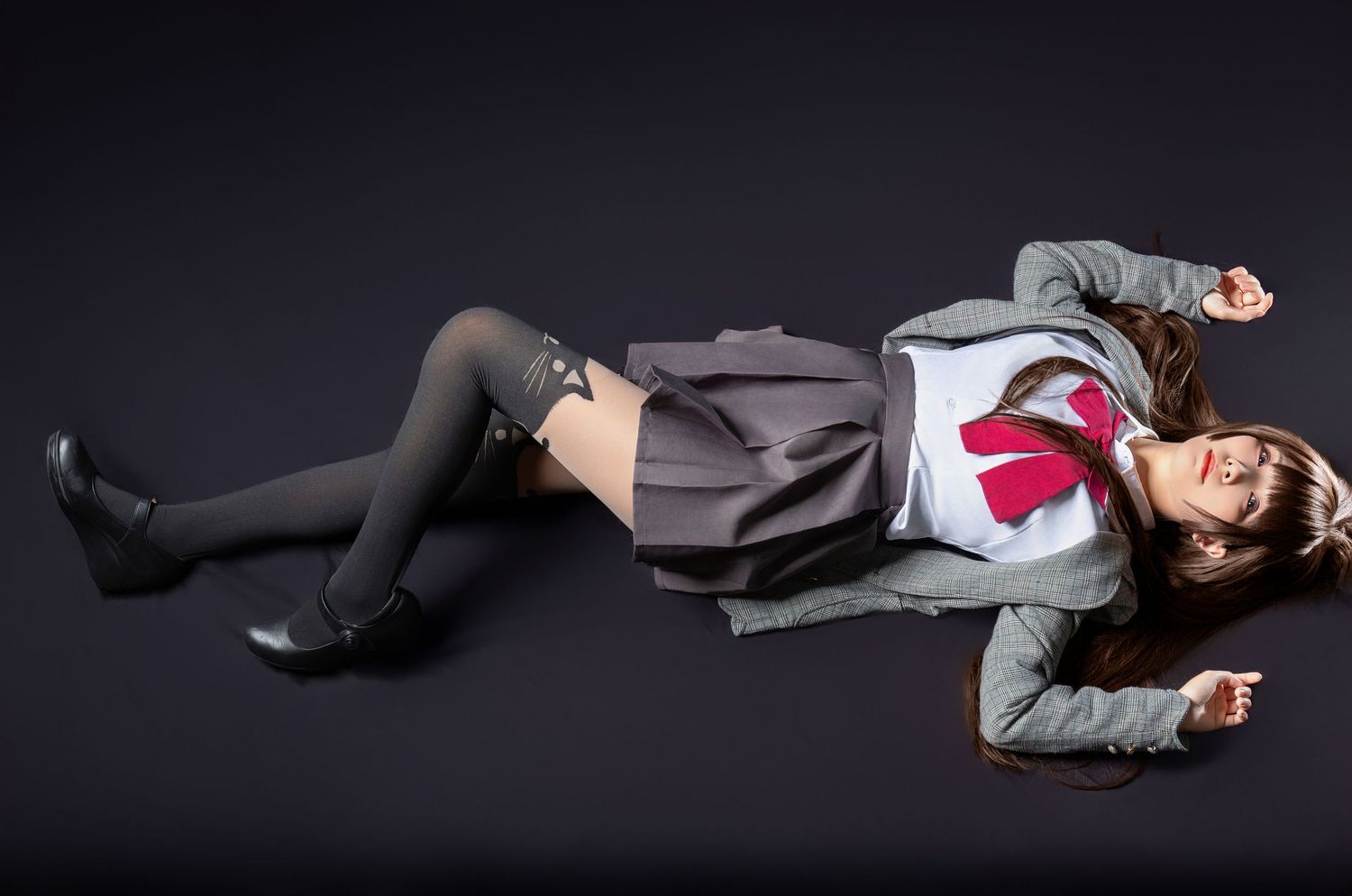 A person in a gray coat and thigh-high stockings lies artistically posed on a dark background.