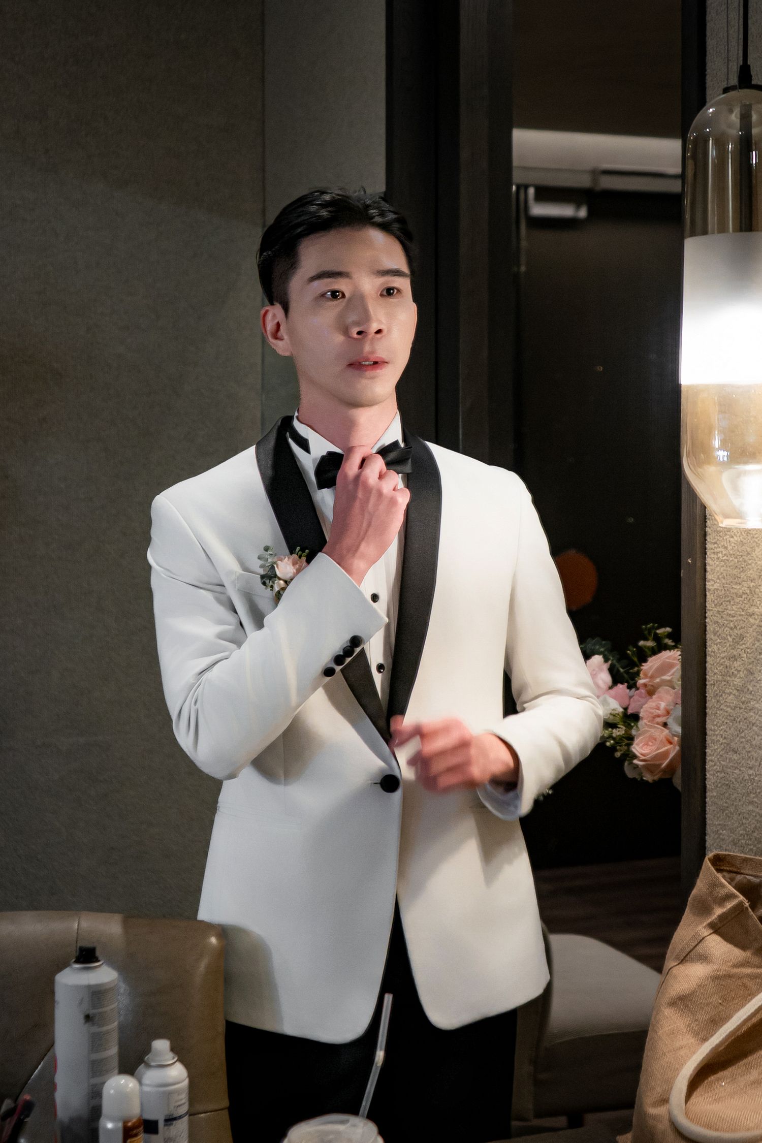 A person wearing a crisp white dinner jacket with black lapels adjusts their tie in an elegant interior setting.