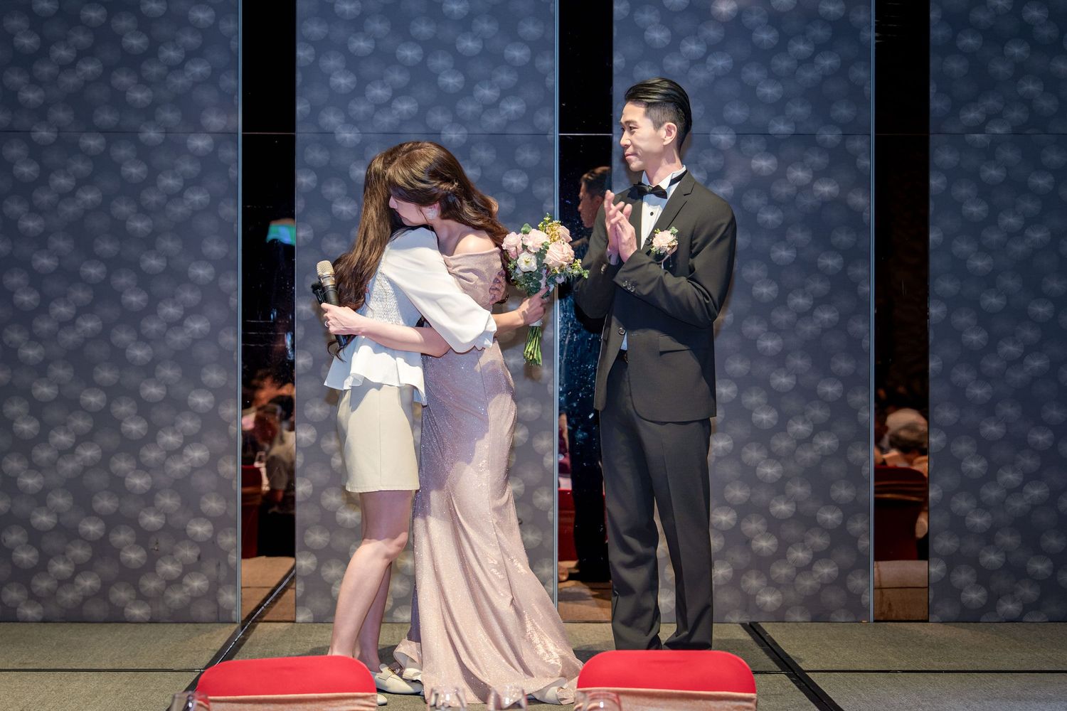 A celebratory moment on stage during a formal event with a red carpet and blue patterned backdrop.