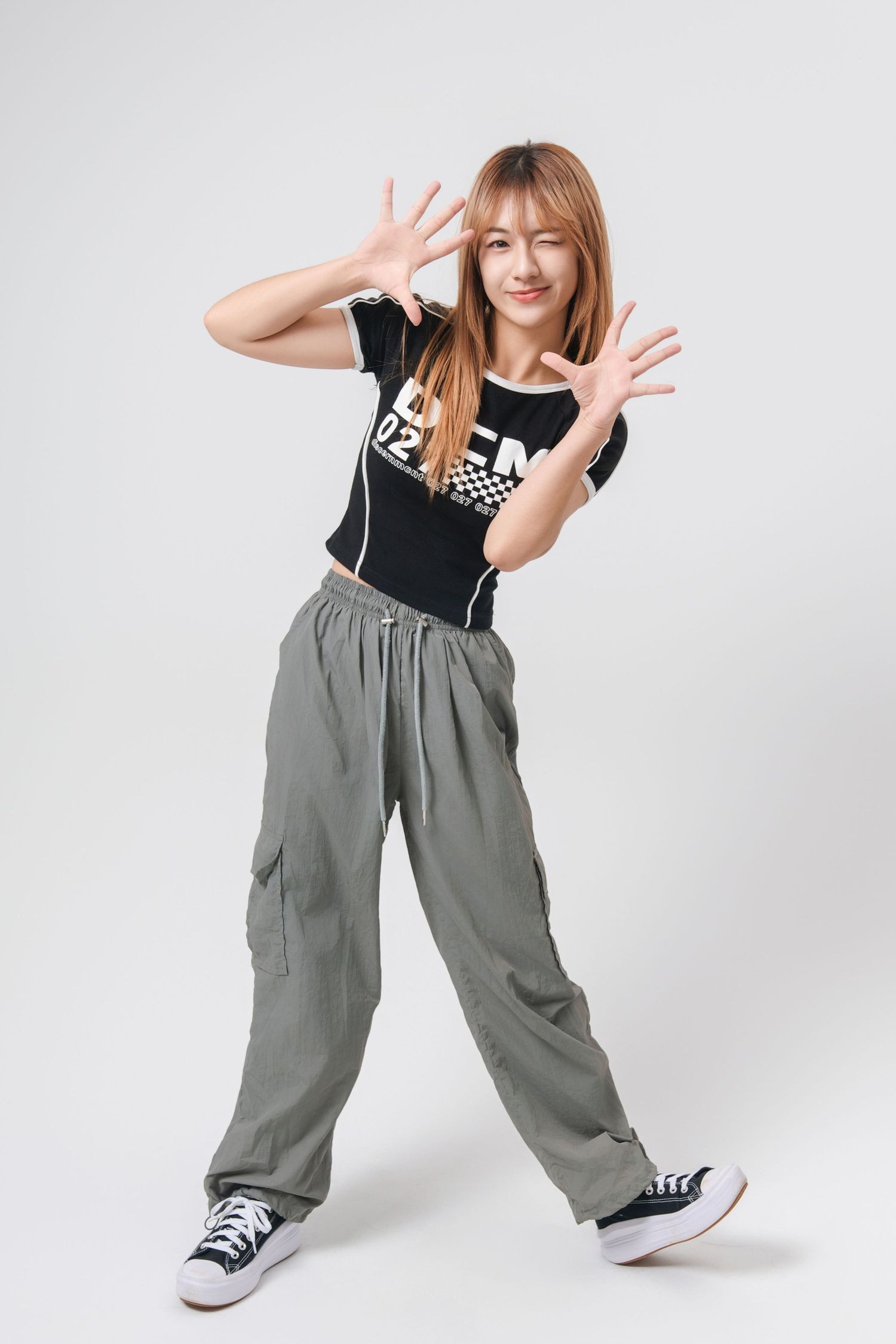 A person in a black t-shirt and baggy gray cargo pants poses playfully against a white background in a photo series.