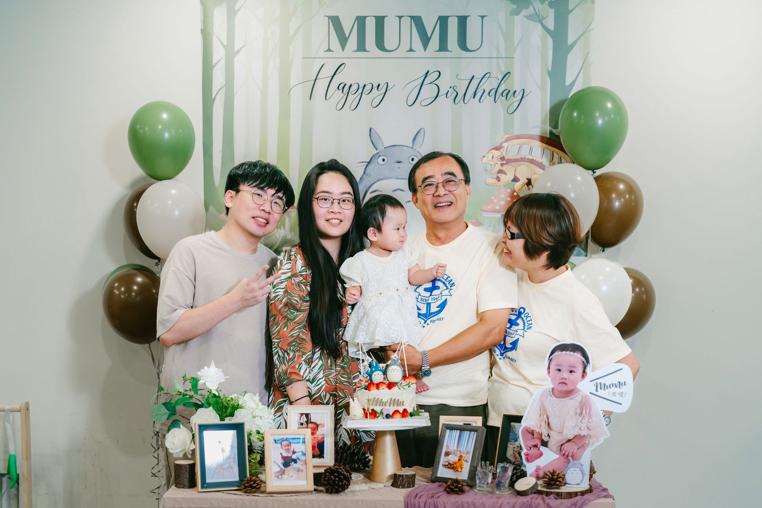 Happy birthday celebration setup with green balloons and photos displayed on a white wall.