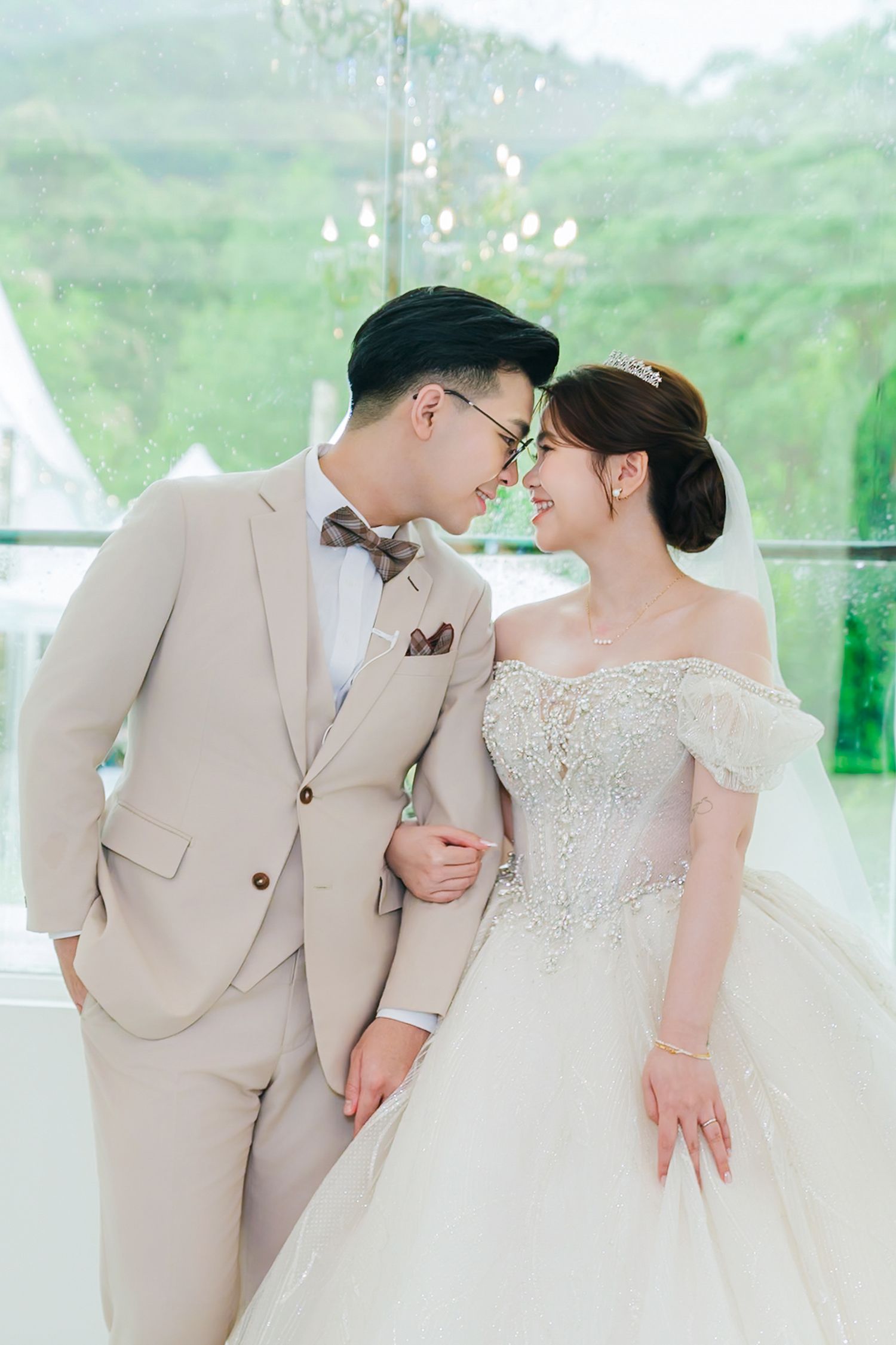 Newlywed couple in elegant beige suit and white lace wedding dress share an intimate moment at their wedding venue.