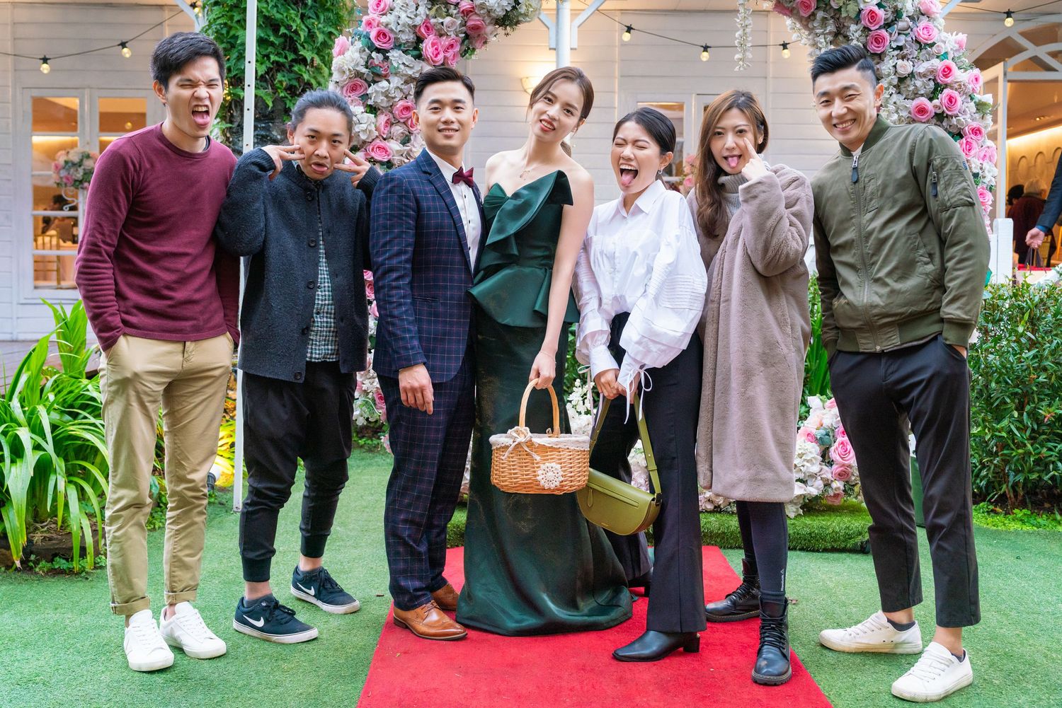 A group of people in casual attire pose together on a red carpet with a decorative floral backdrop.