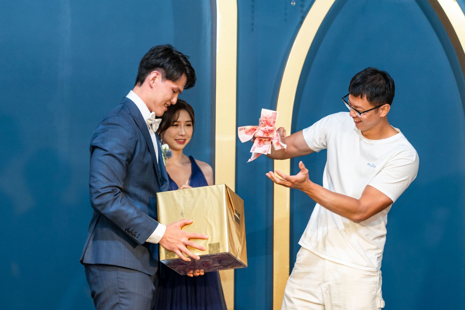 Three people stand against a blue wall, with one person in a suit holding a bag while another examines a small pink item.