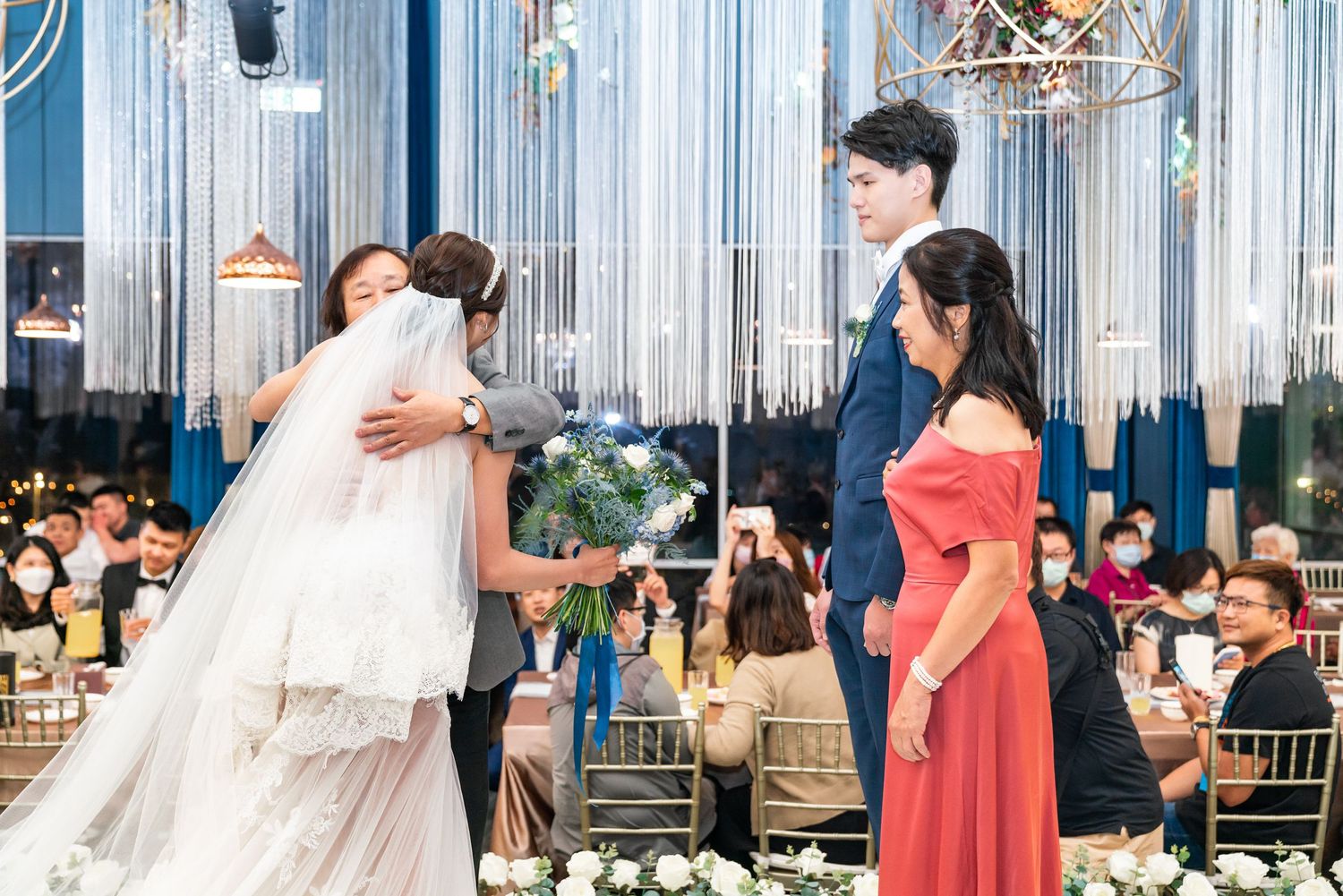 Wedding celebration in an elegant ballroom decorated with shimmering blue curtains and crystal chandeliers.