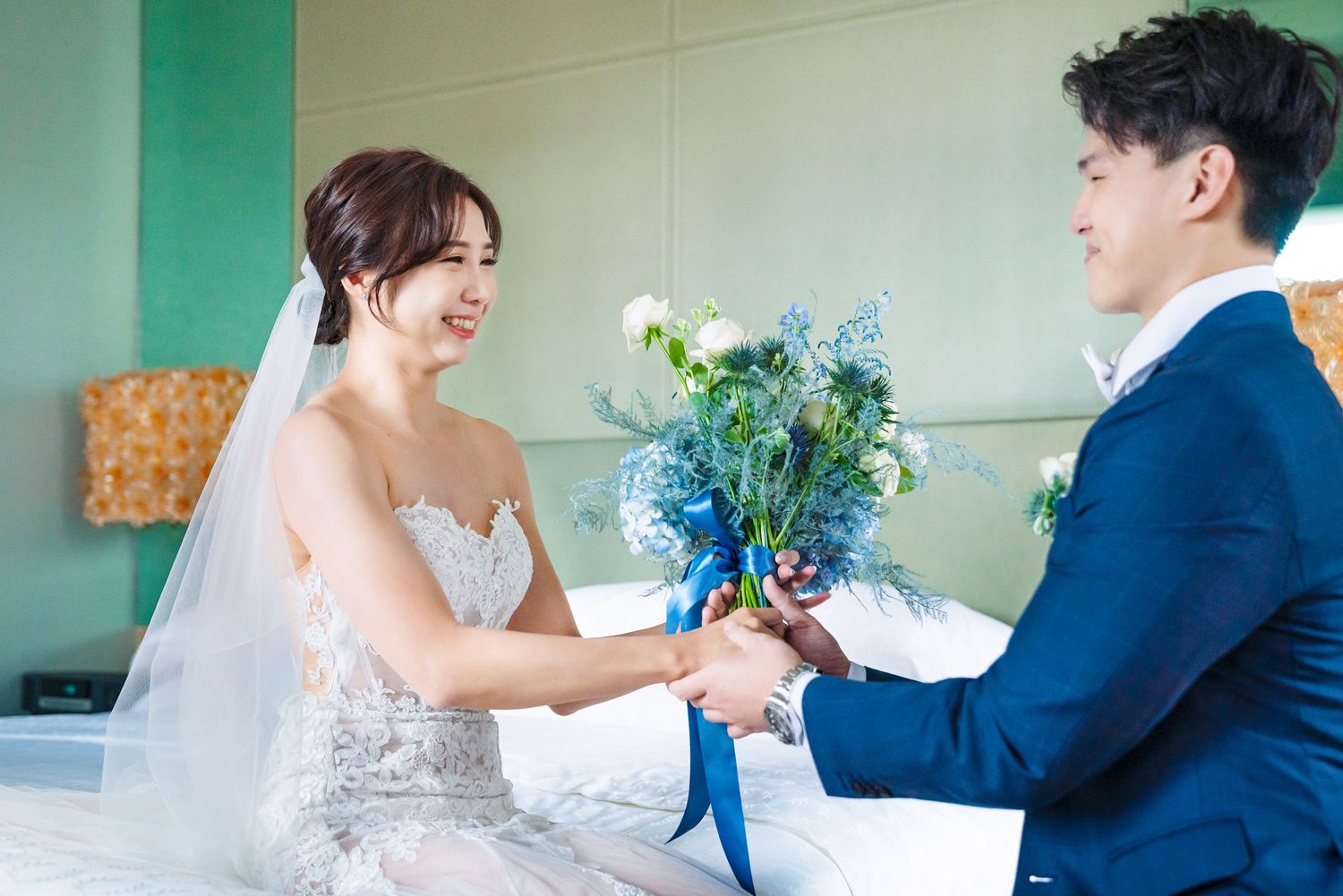 A bride in a white wedding dress receives a vibrant blue and green floral bouquet during a sunny wedding ceremony.