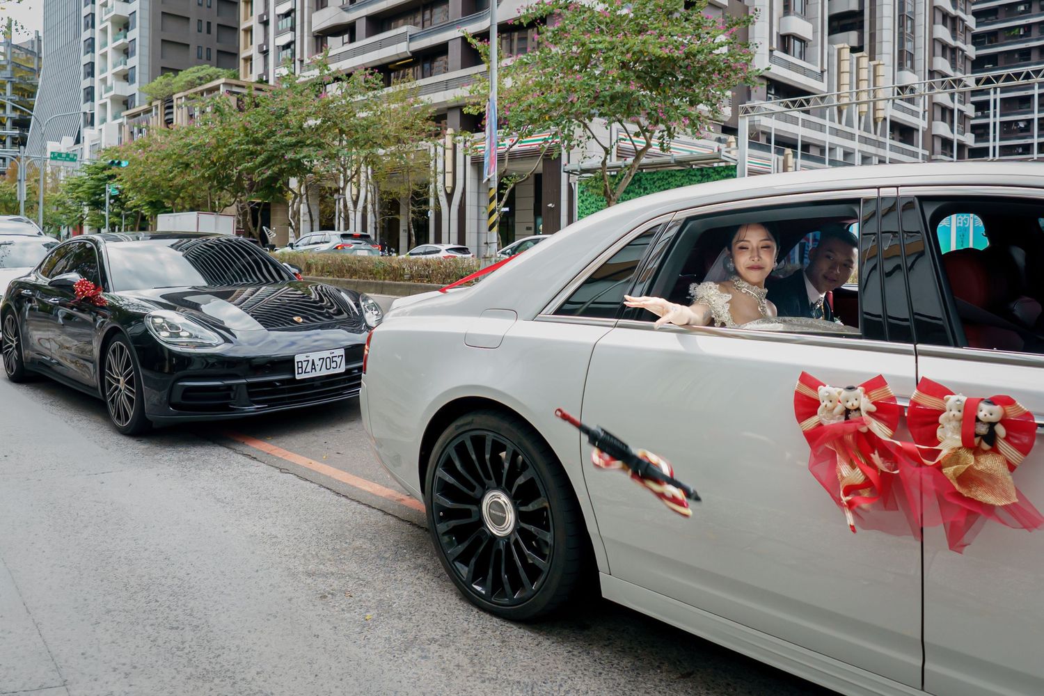 A series of luxury wedding cars decorated with red ribbons parked along a city street.