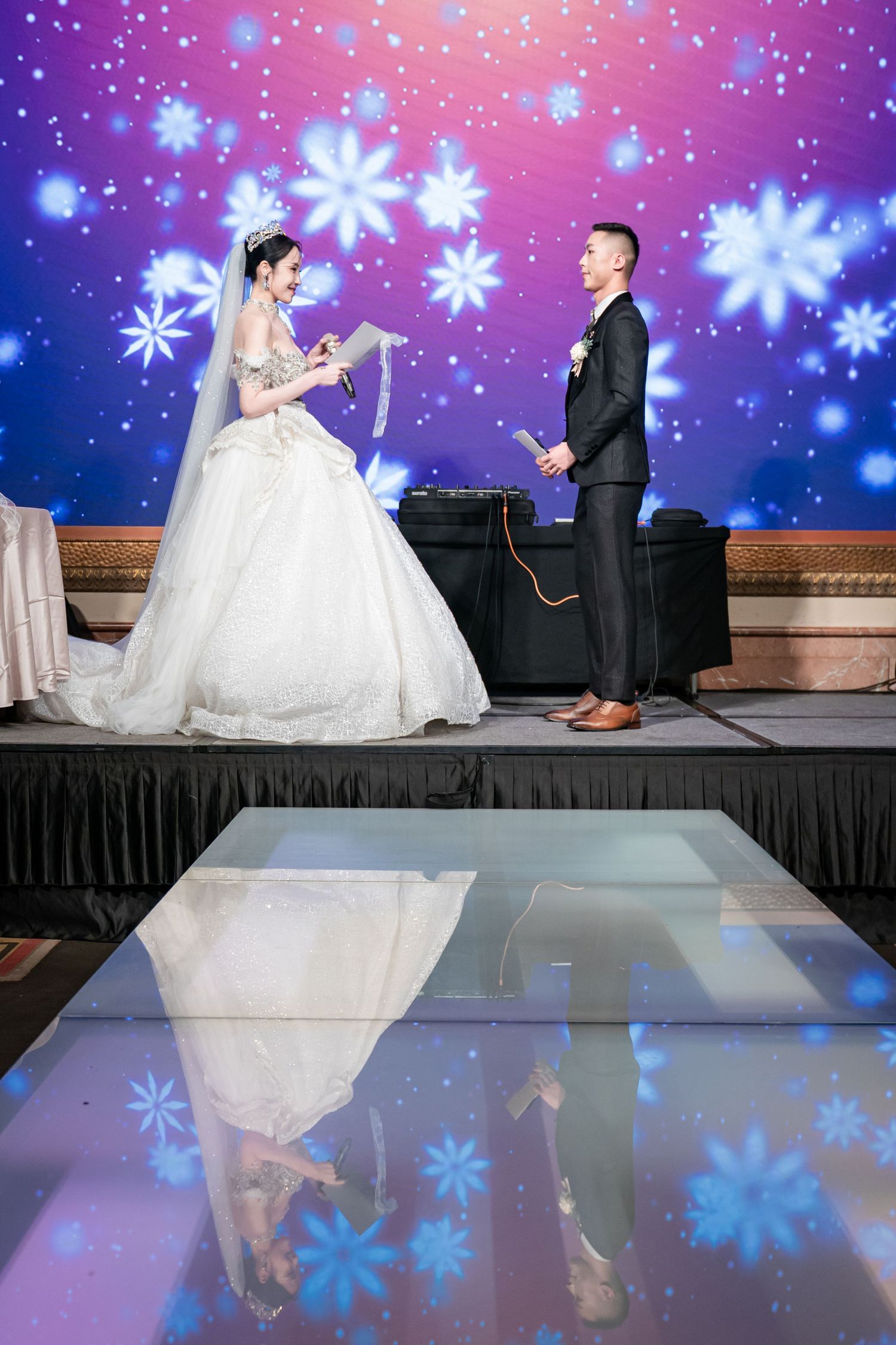 A couple stands on stage during a winter-themed wedding ceremony with blue snowflake projections in the background.