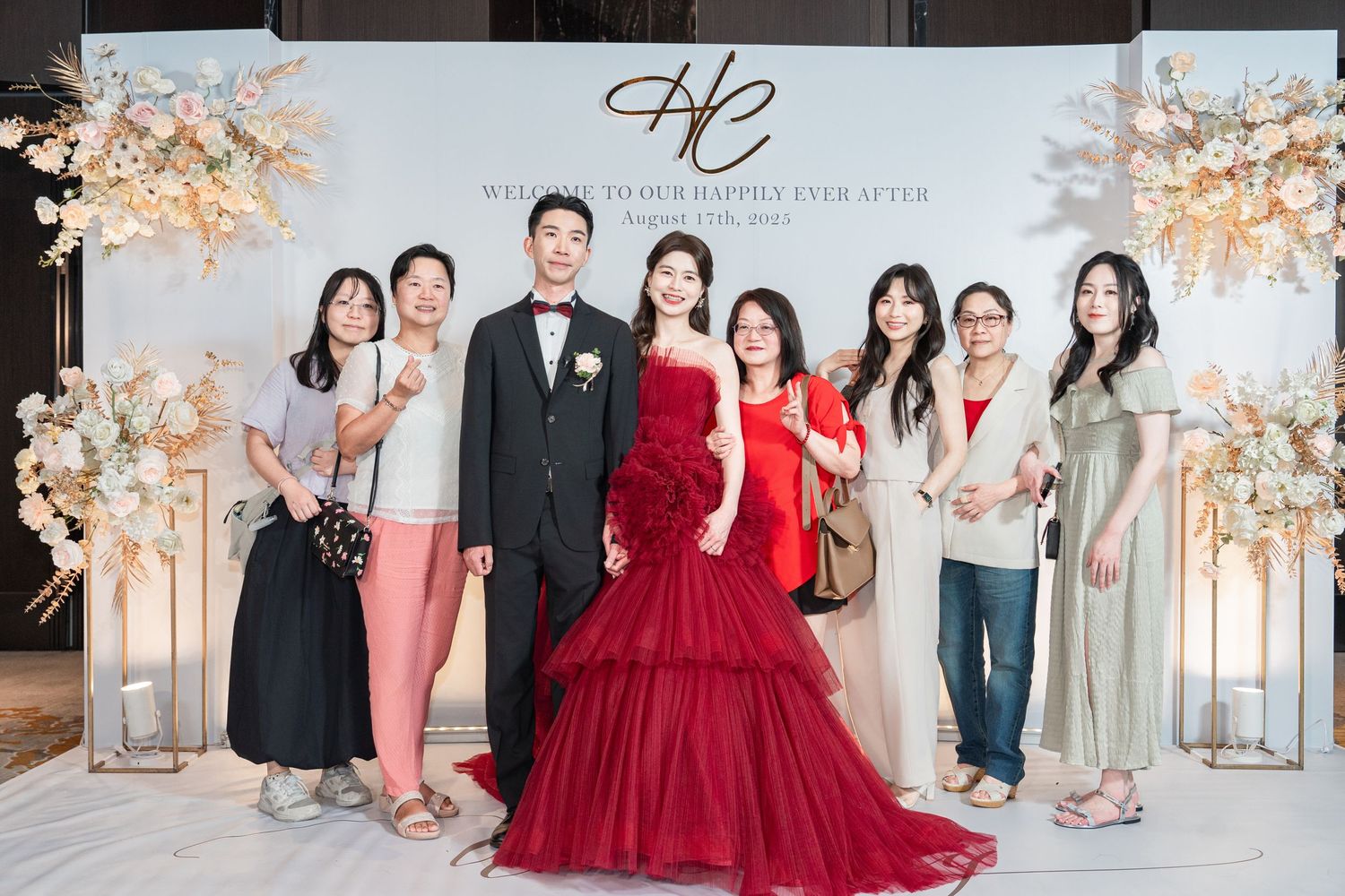 A group photo at an elegant wedding event with attendees in formal attire including red and pink dresses.