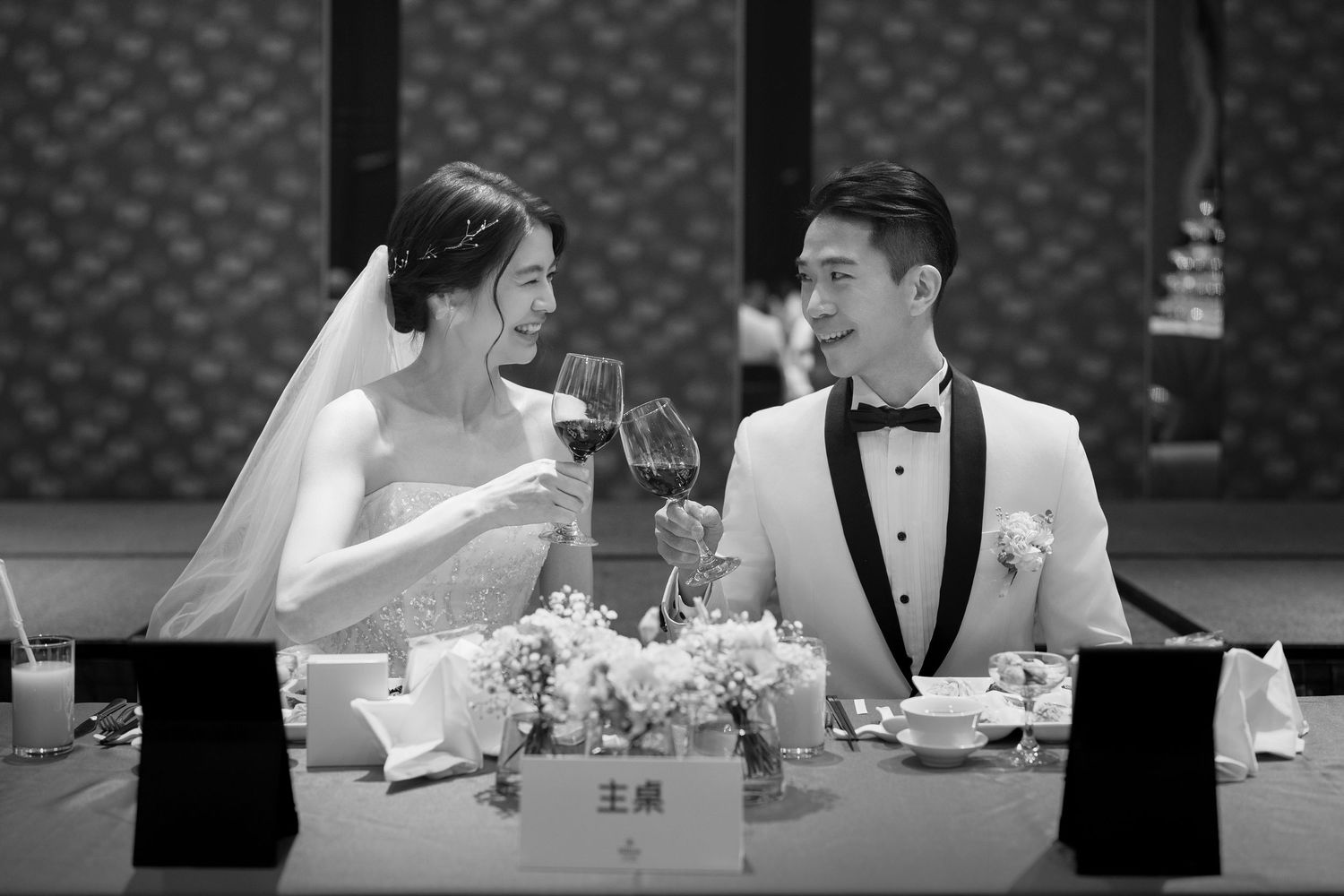 Wedding couple sharing an intimate moment at a formal reception dinner table while toasting with wine glasses.