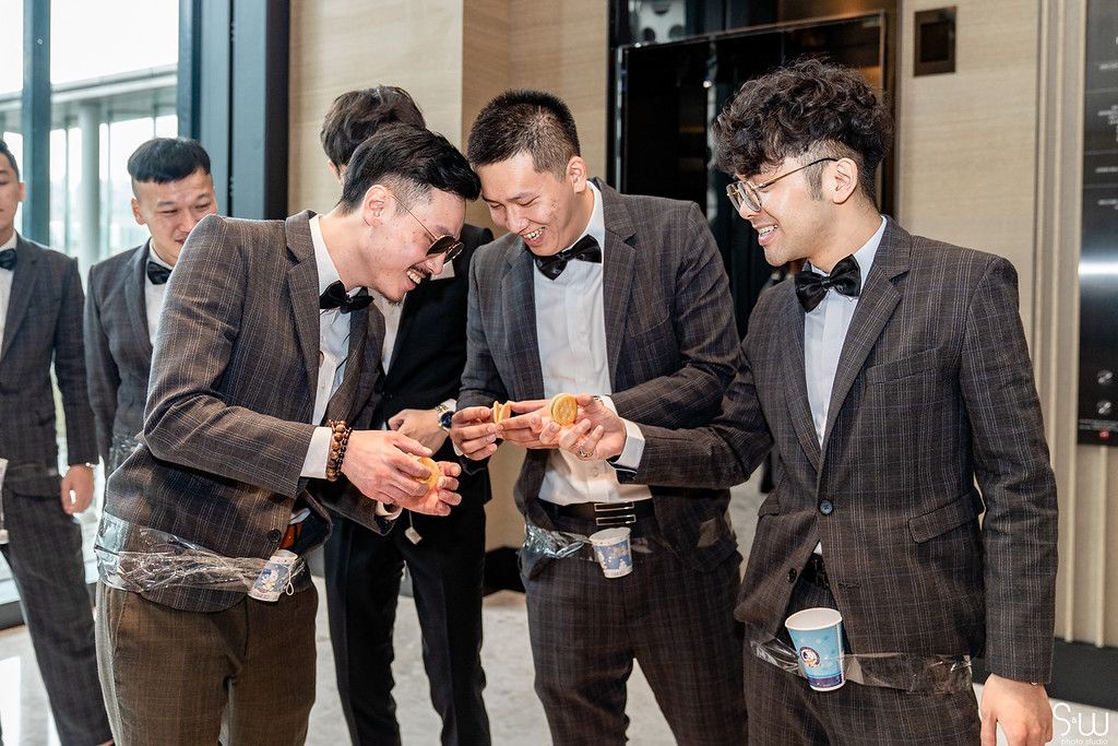 Groomsmen in suits gather around to look at something on a mobile device.
