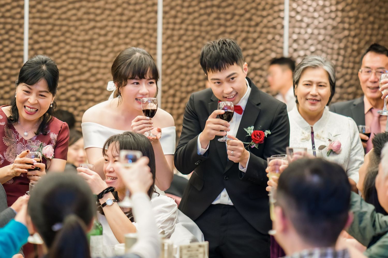 Wedding banquet scene with guests sharing drinks and laughter around dining tables.