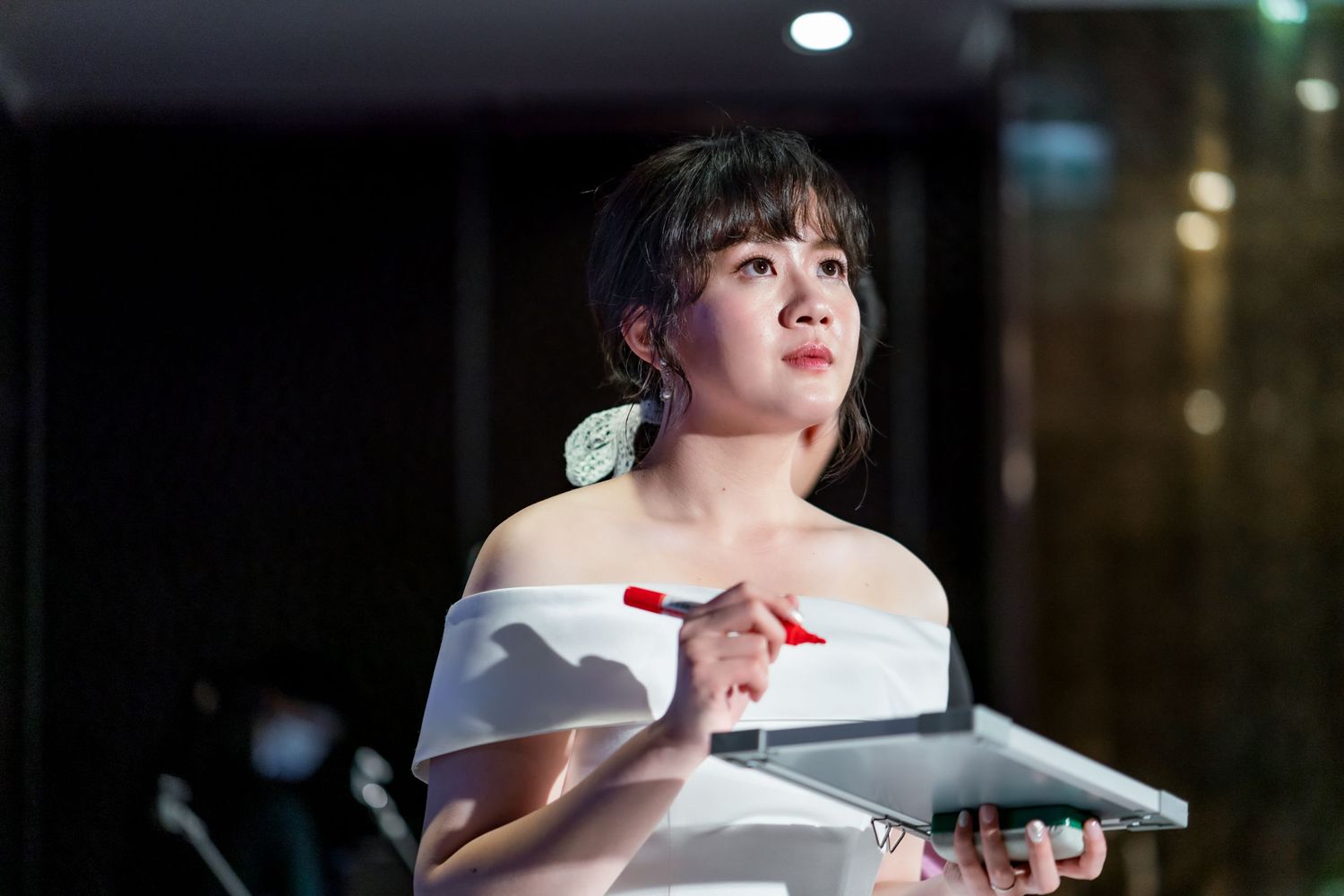 Person in white off-shoulder dress holds a tablet during an indoor event.