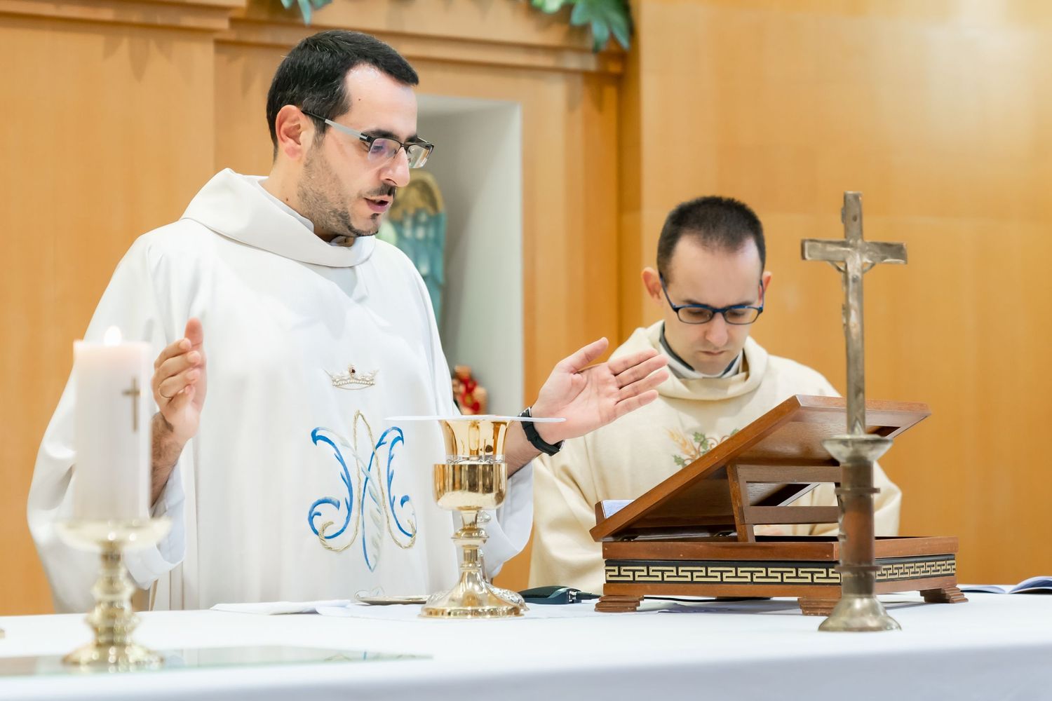 Priests conducting Catholic mass ceremony at altar with chalice and liturgical items.
