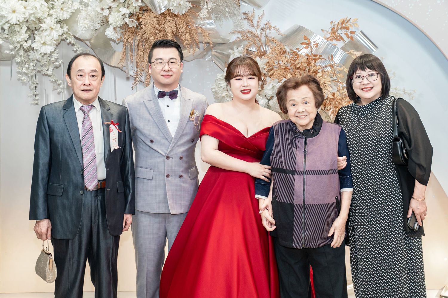 Group photo at formal event with people wearing elegant attire including red gowns and suits.