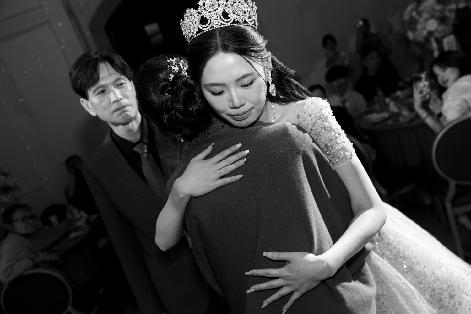 A black and white photo of a bride in a tiara and gown at an elegant wedding celebration.