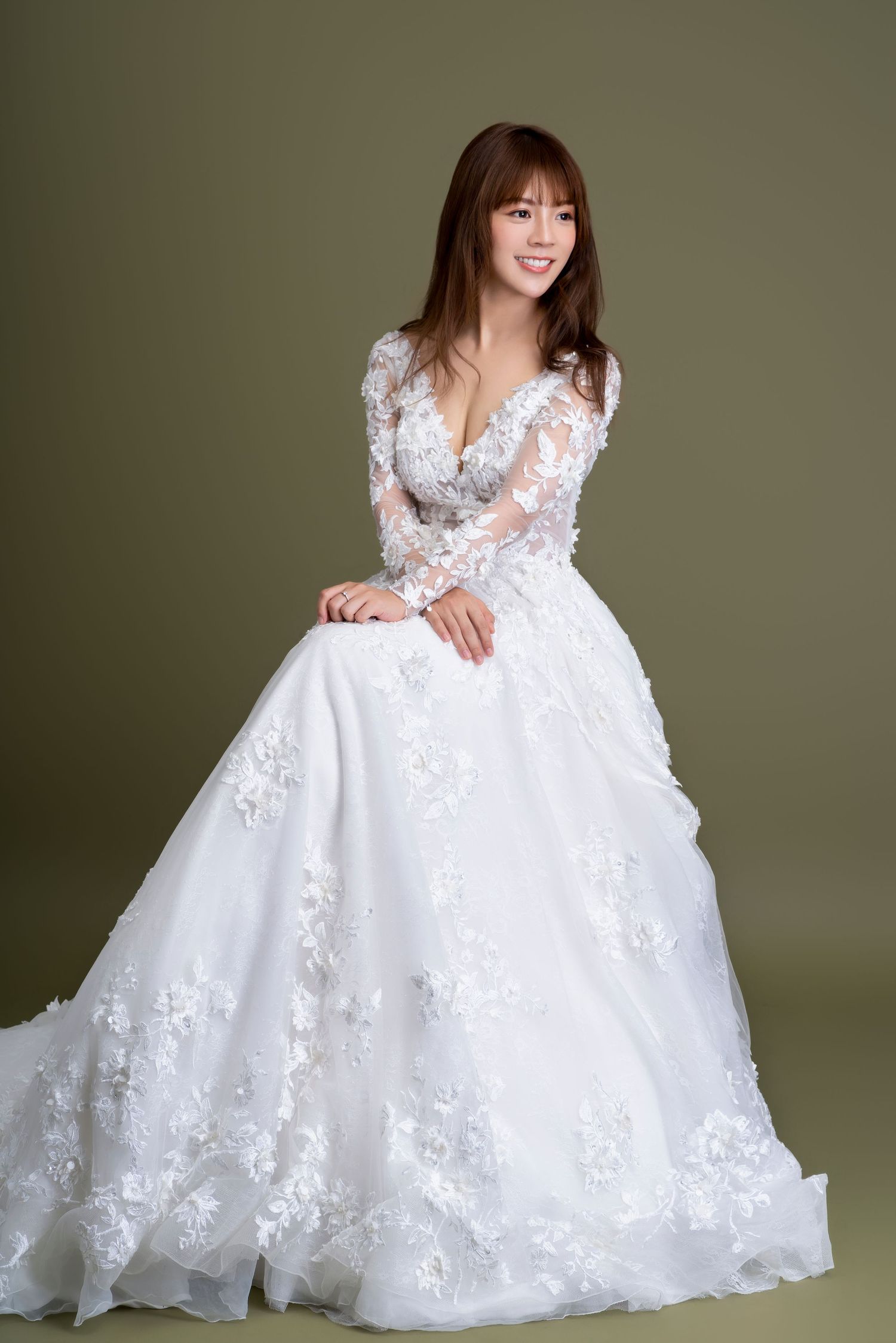 A stunning white wedding gown with long lace sleeves and floral appliques photographed against an olive green backdrop.
