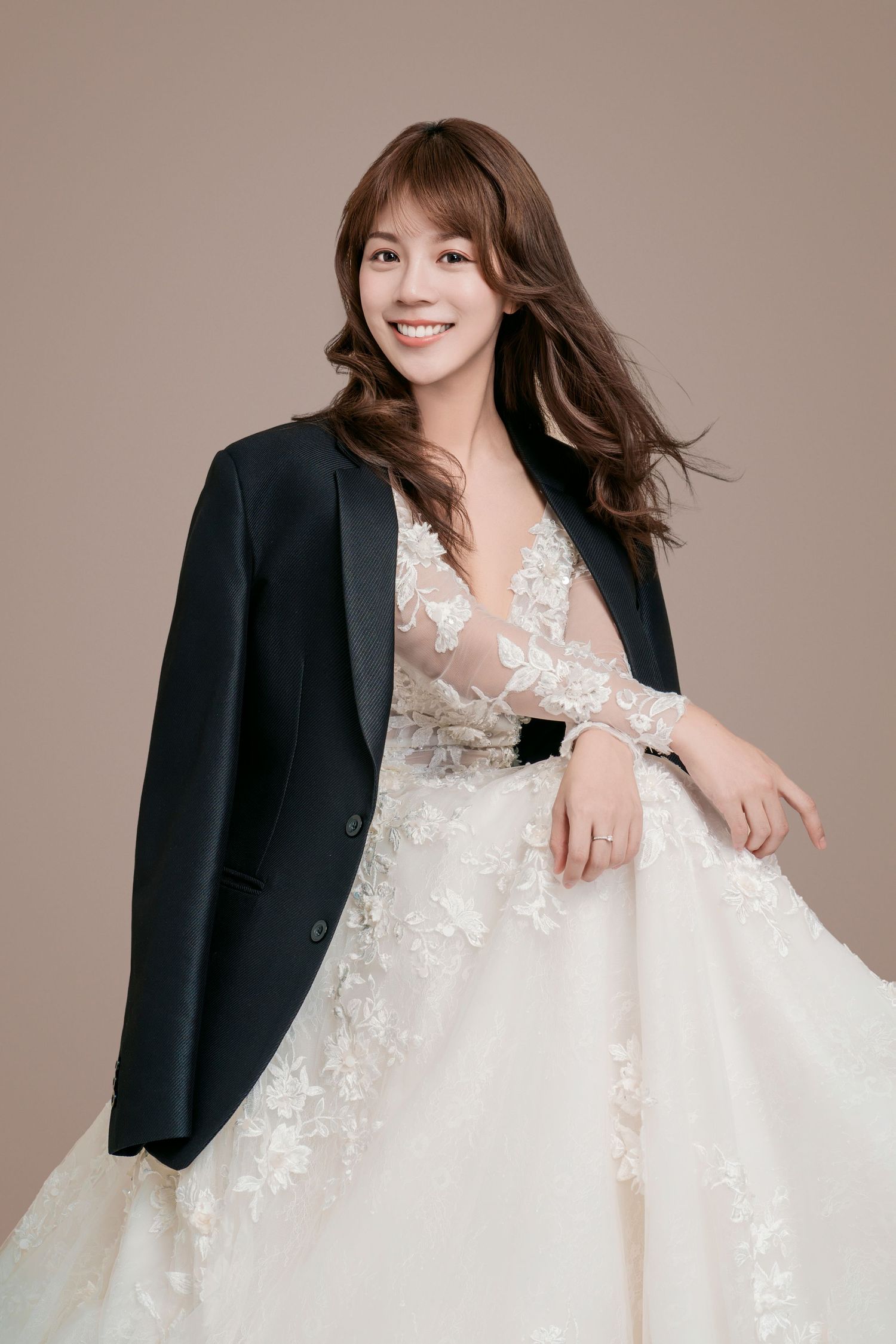 Elegant wedding fashion portrait featuring a white lace gown paired with a classic black blazer against a neutral backdrop.